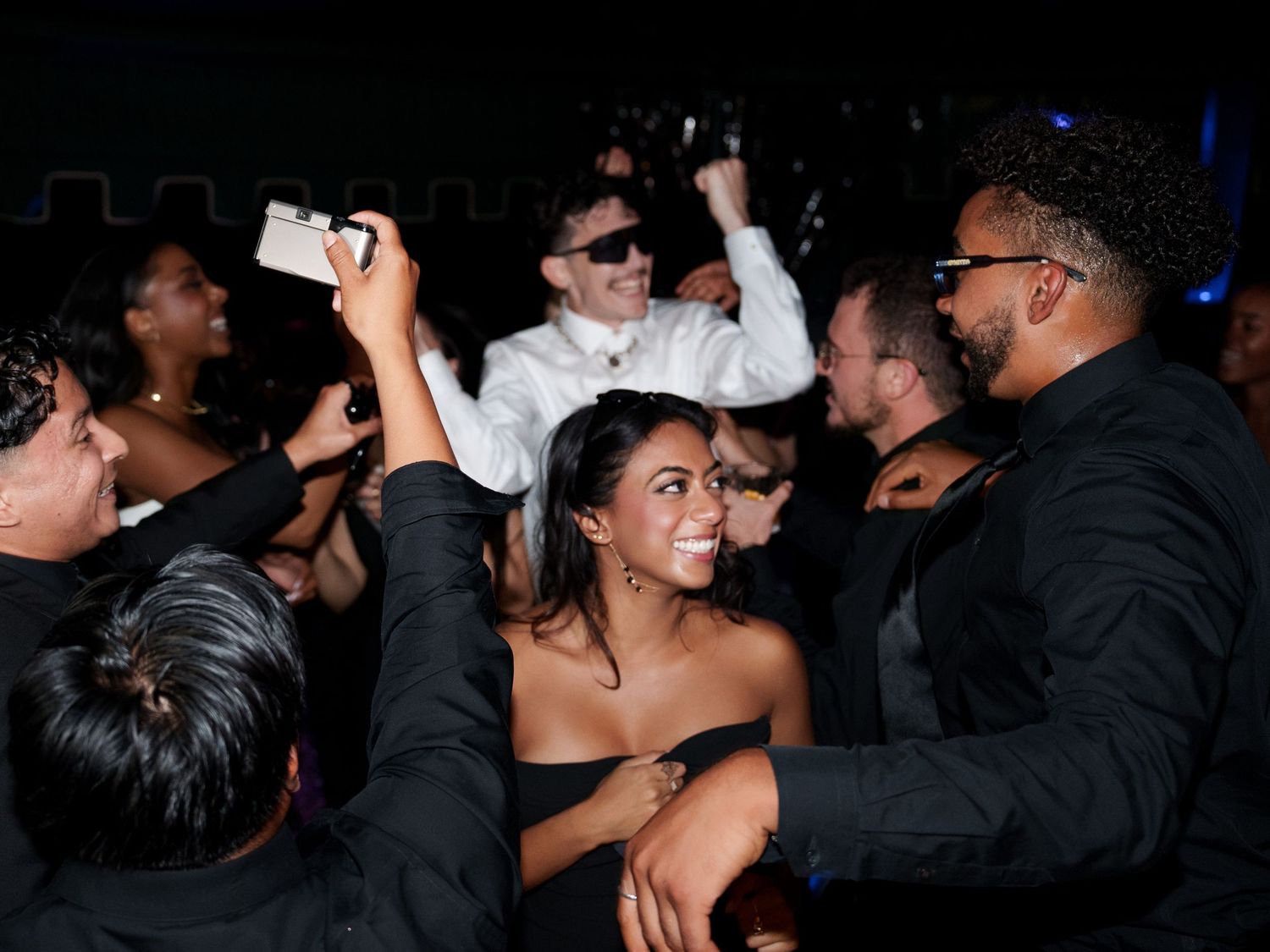 A crowded nightclub scene with people dancing and socializing under blue lighting.
