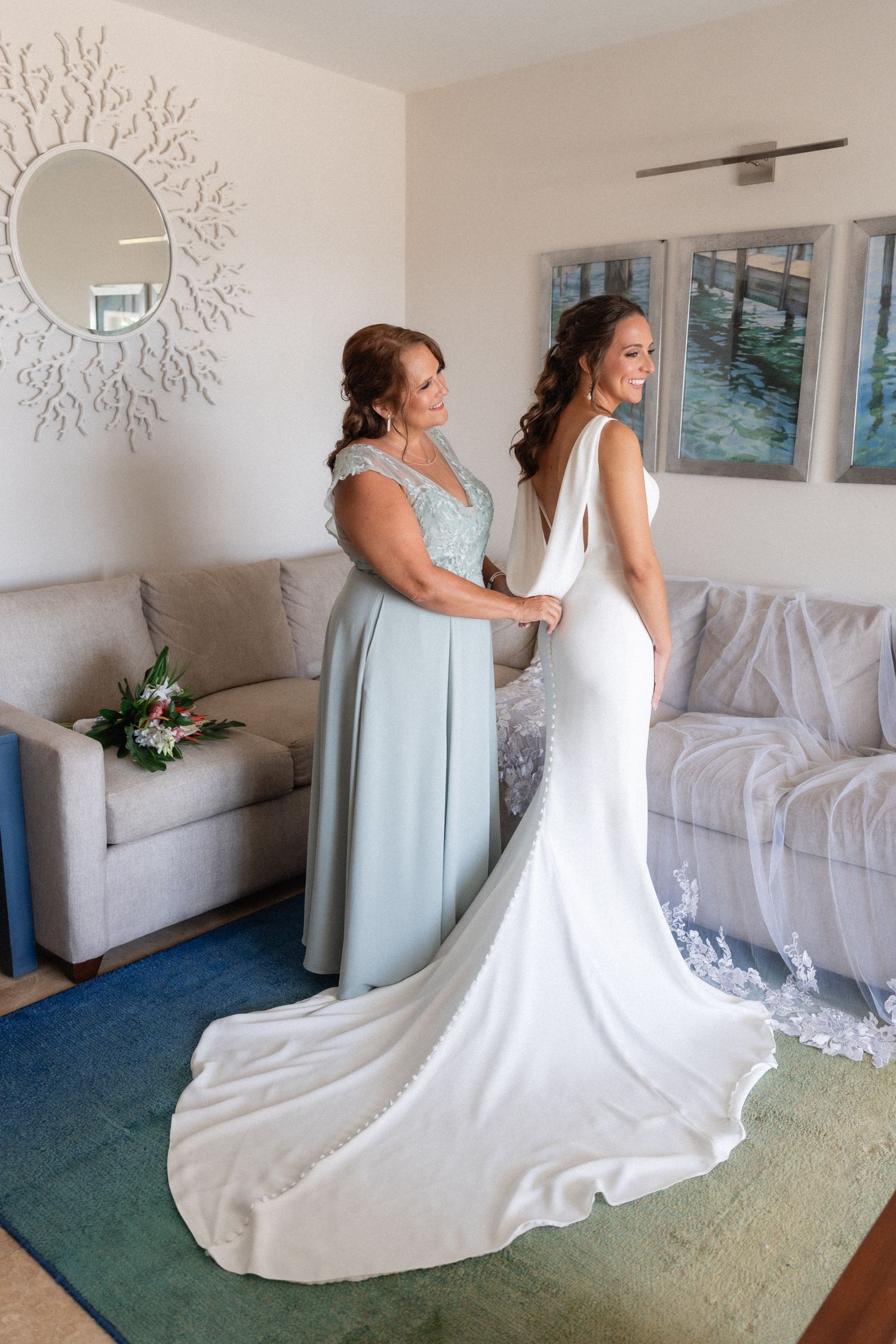 Wedding dress fitting scene in elegant room with sunburst mirror and coastal artwork.