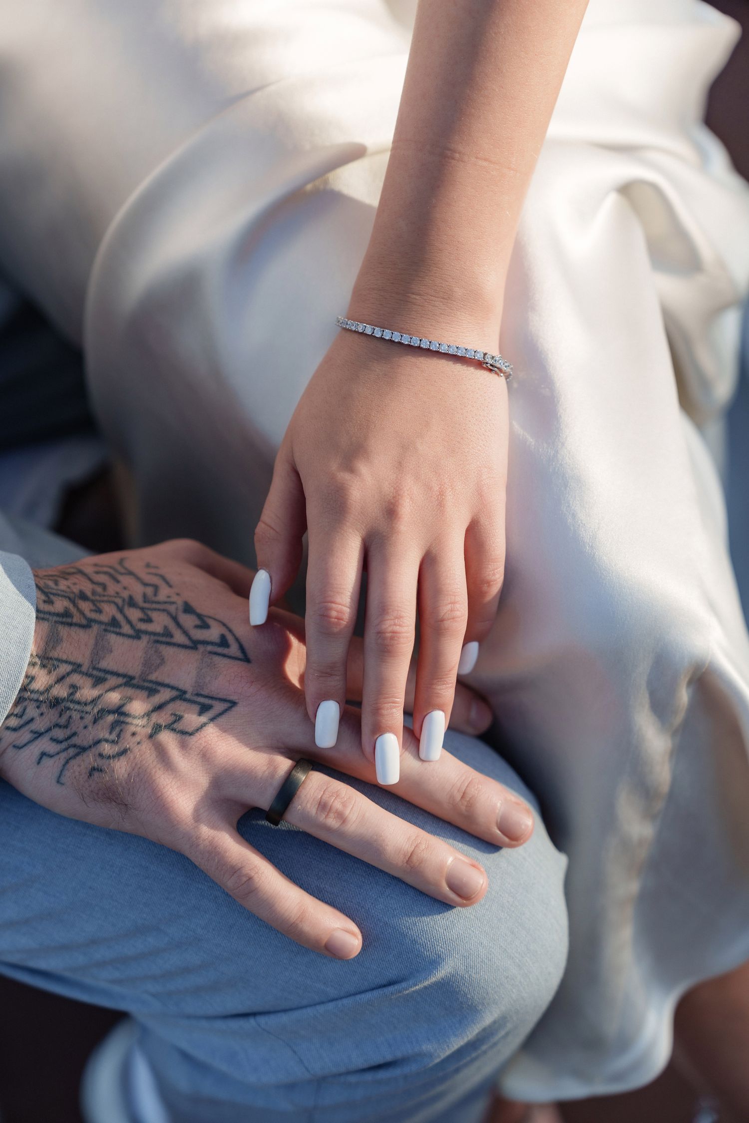 Close-up of hands with light blue nails and a delicate bracelet against a white dress.