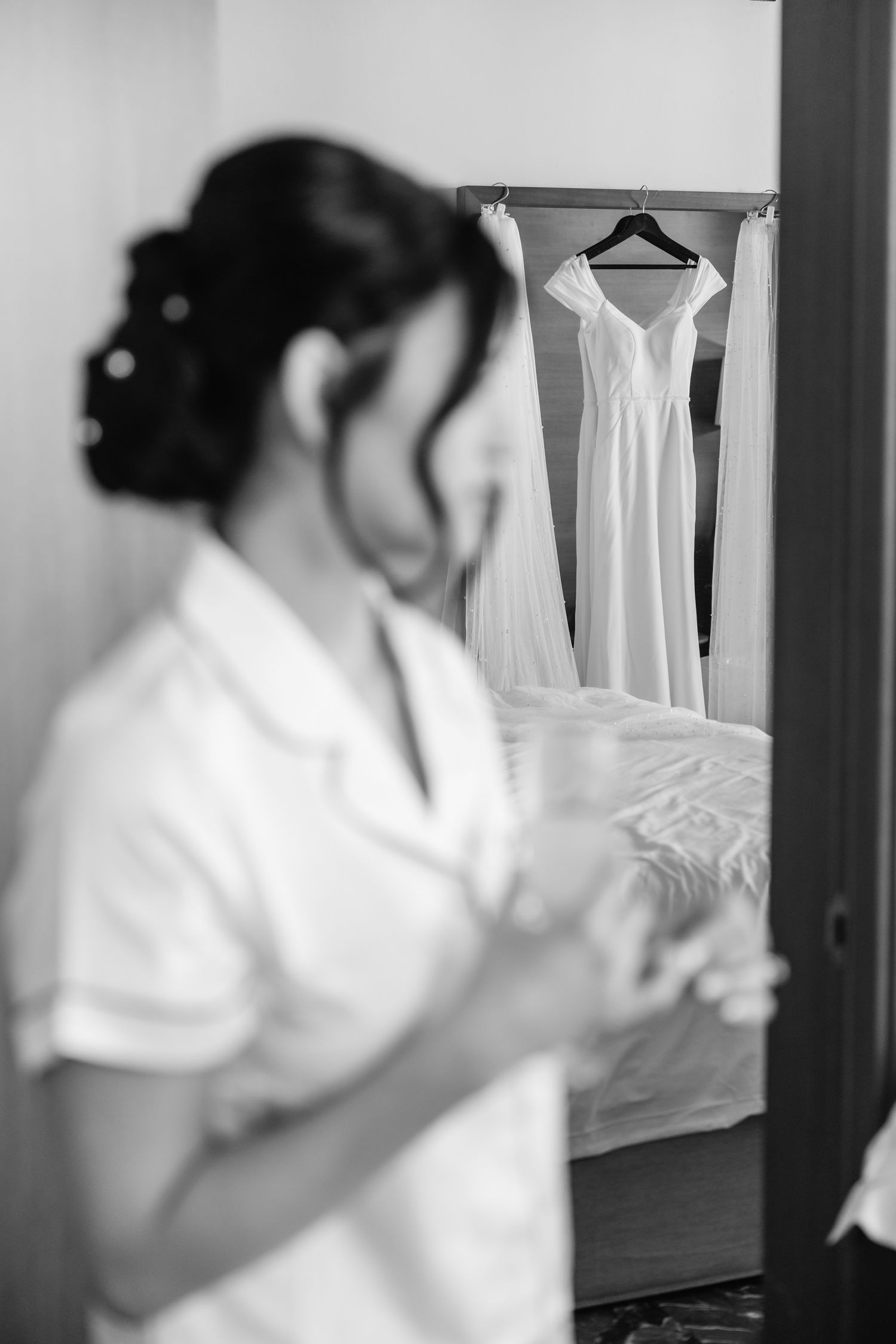 Black and white image of wedding preparations with a dress hanging in the background.