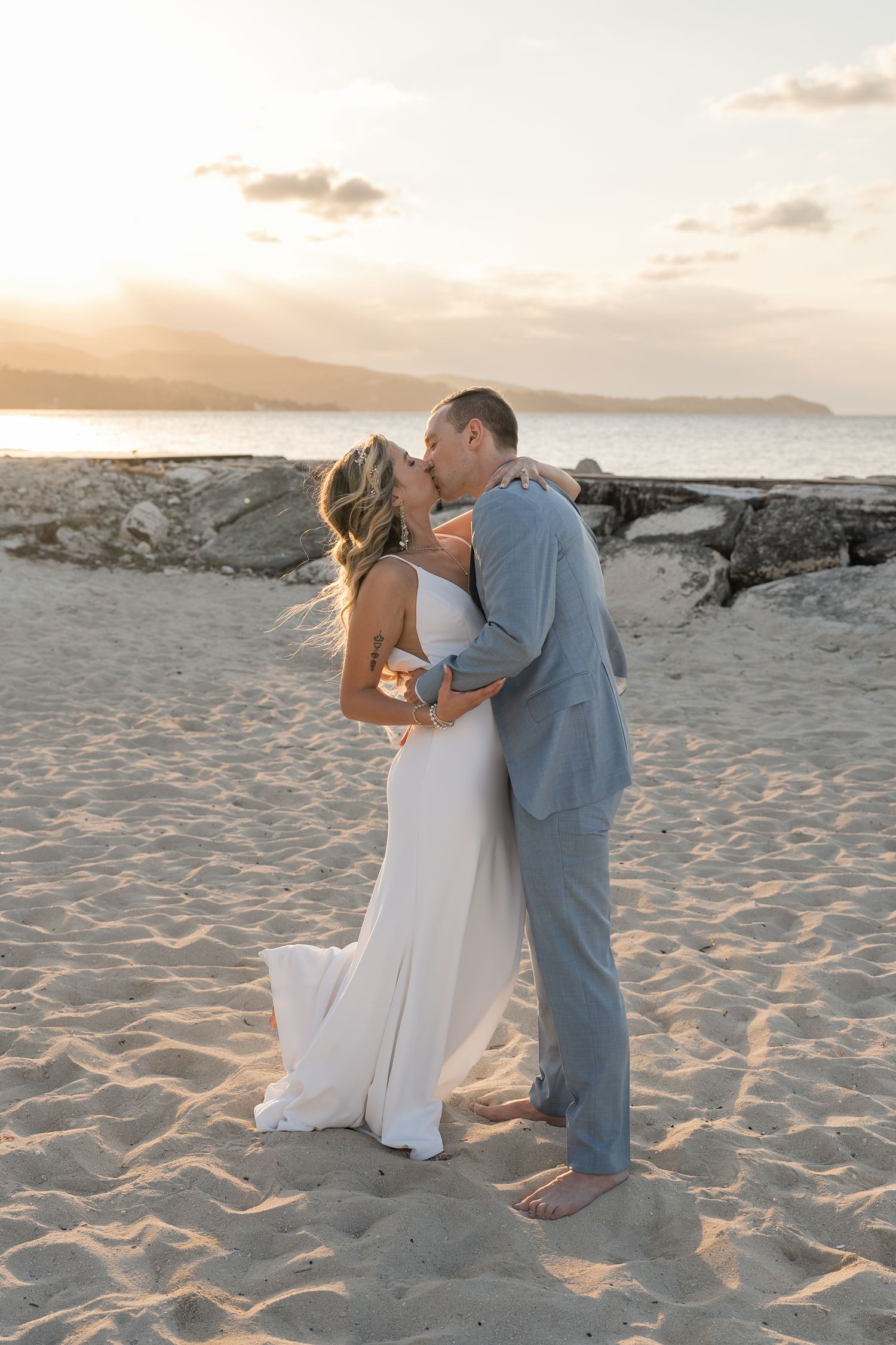 A romantic moment between newlyweds on a beach during golden hour with mountains in the distance.