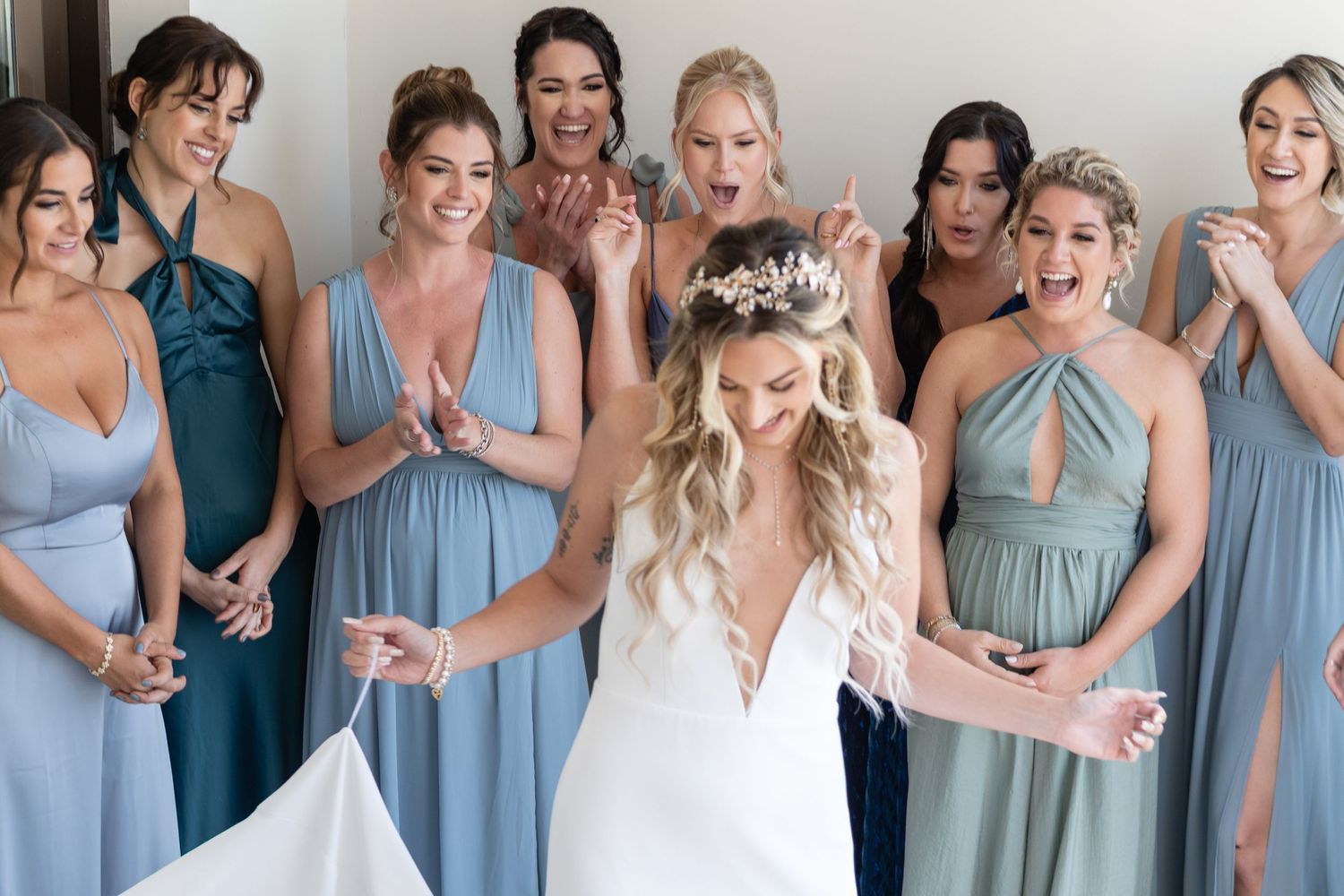 A bridal party in light blue dresses shares a joyful moment together indoors.