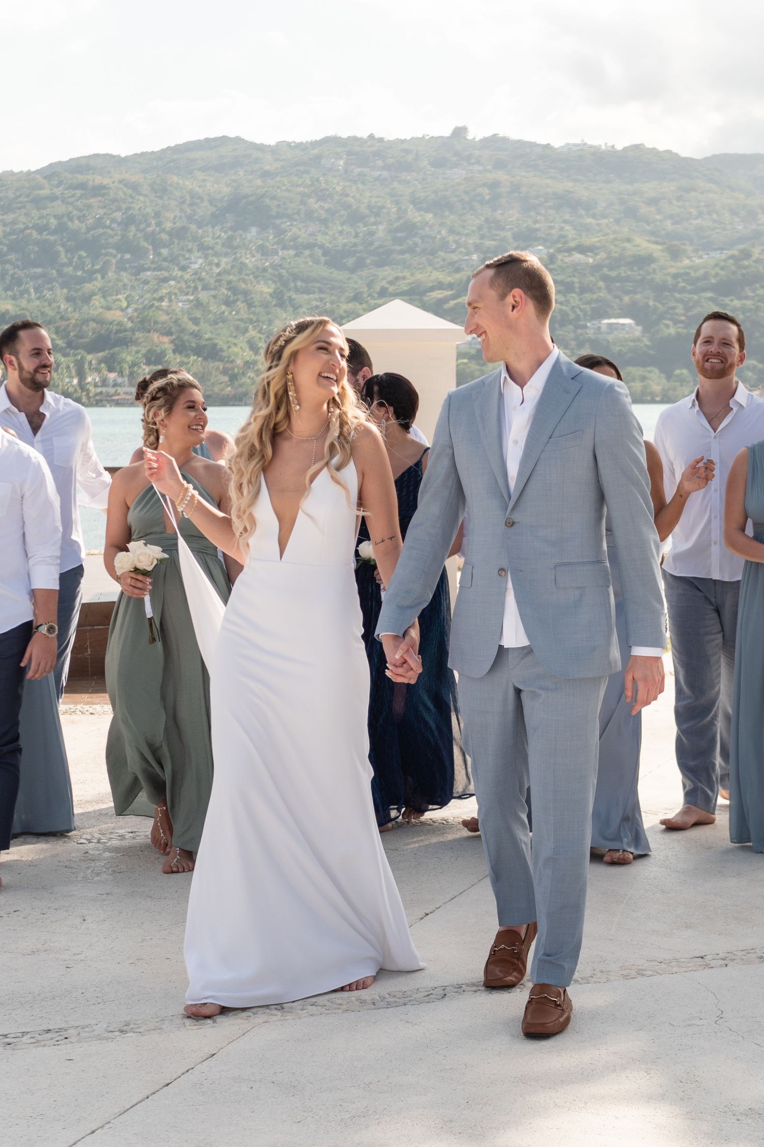 Newlyweds walking hand in hand with wedding party on tropical terrace.