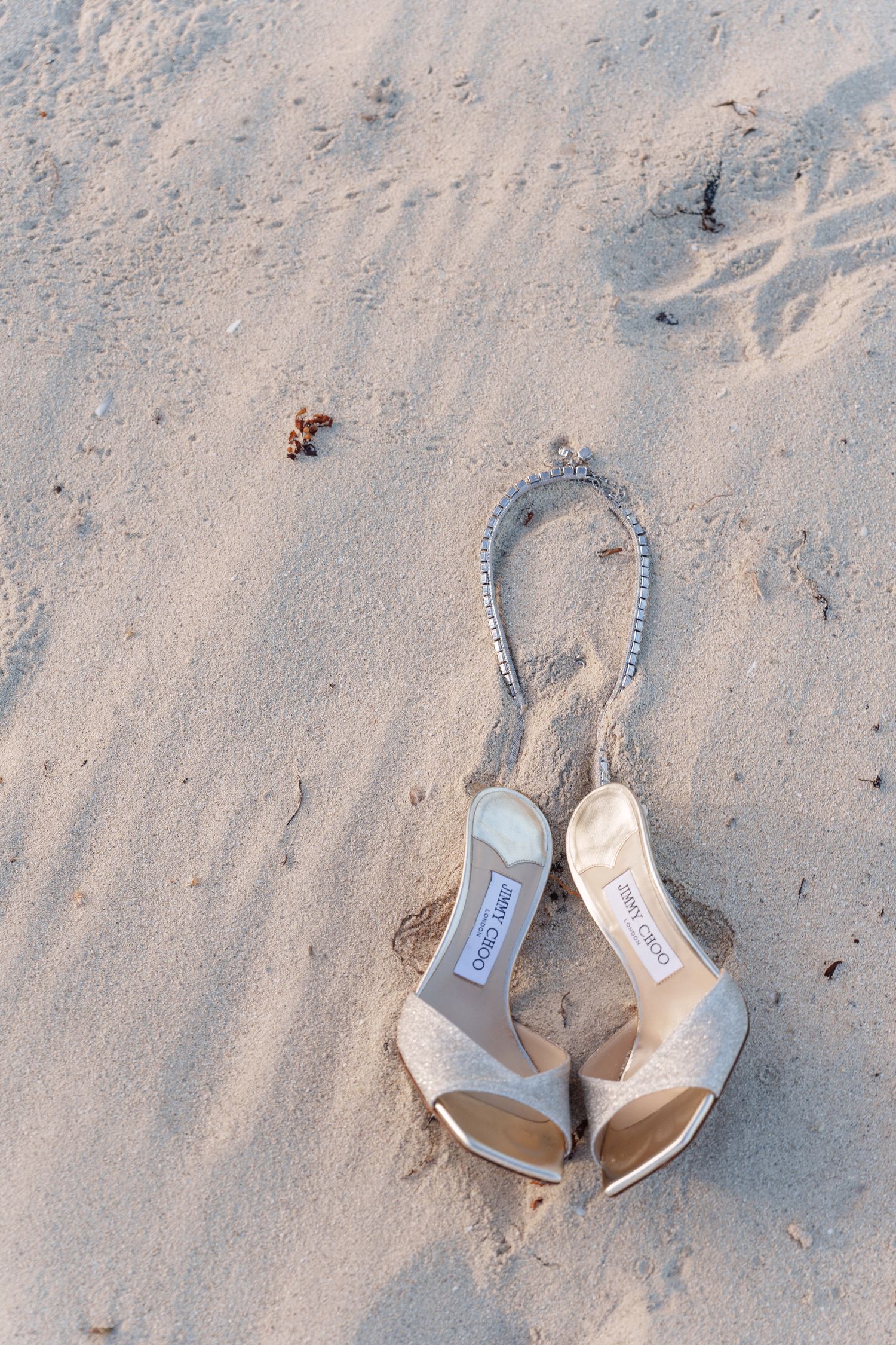 A pair of elegant beige wedding shoes placed on soft beach sand.