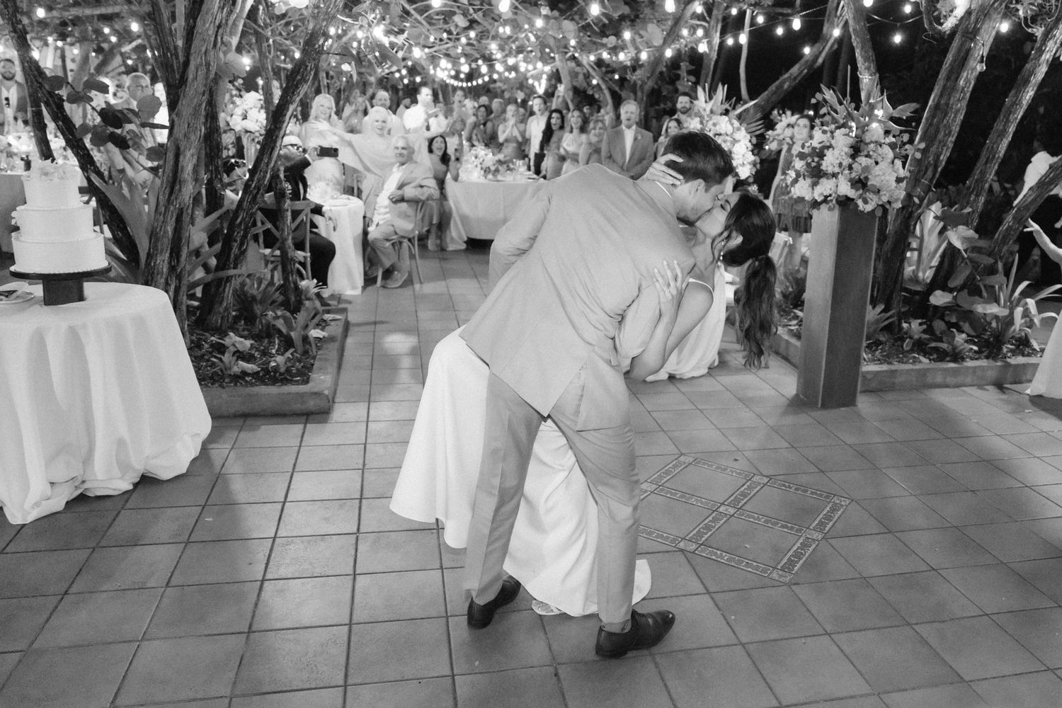 A black and white photo captures joyful dancing at an outdoor wedding reception.