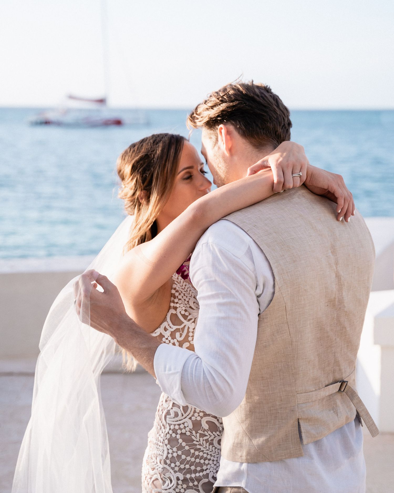An intimate embrace on a beachfront with formal wedding attire and ocean backdrop.