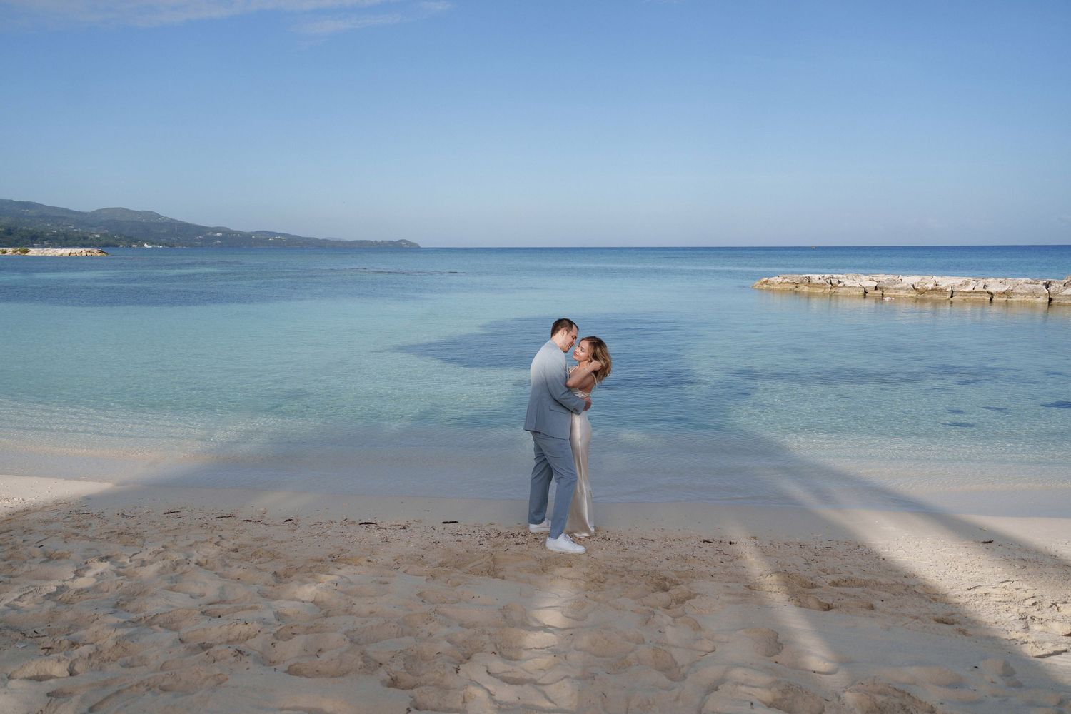 A couple shares an intimate embrace on a beautiful Caribbean beach with crystal clear waters.