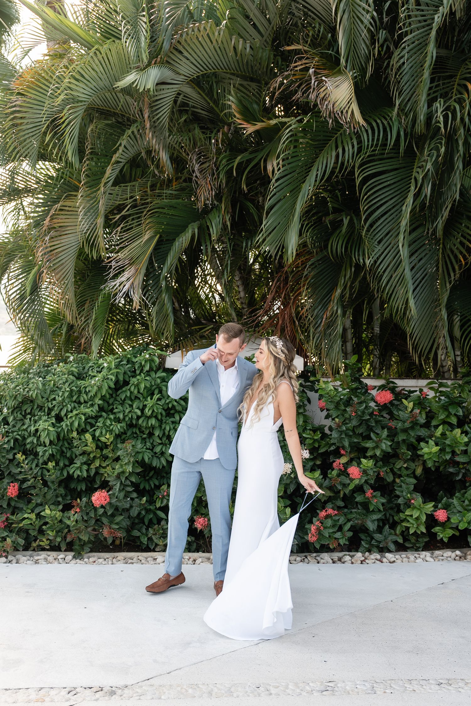 A celebratory wedding pose beneath towering palm trees and pink flowers.