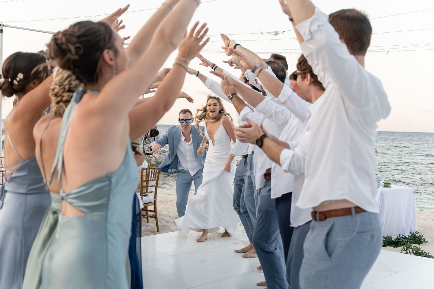 Wedding guests dancing and celebrating with raised arms at a beachside reception.