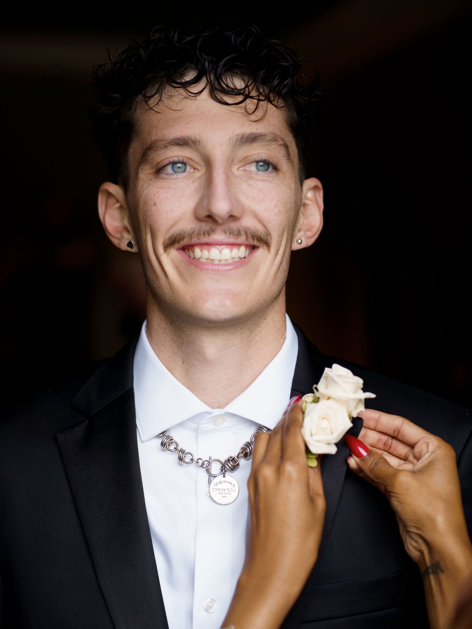 A boutonniere being pinned onto a white dress shirt during formal wedding preparations.