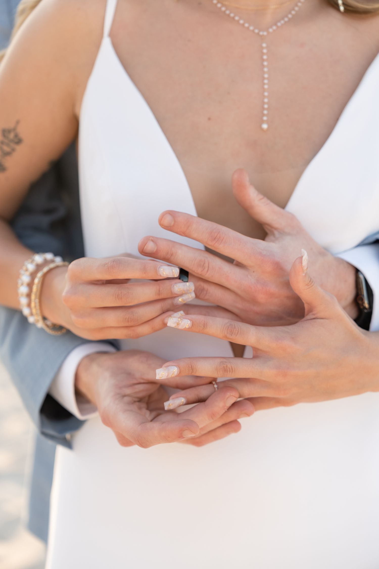 Close up of hands exchanging rings with delicate jewelry and white dress details.