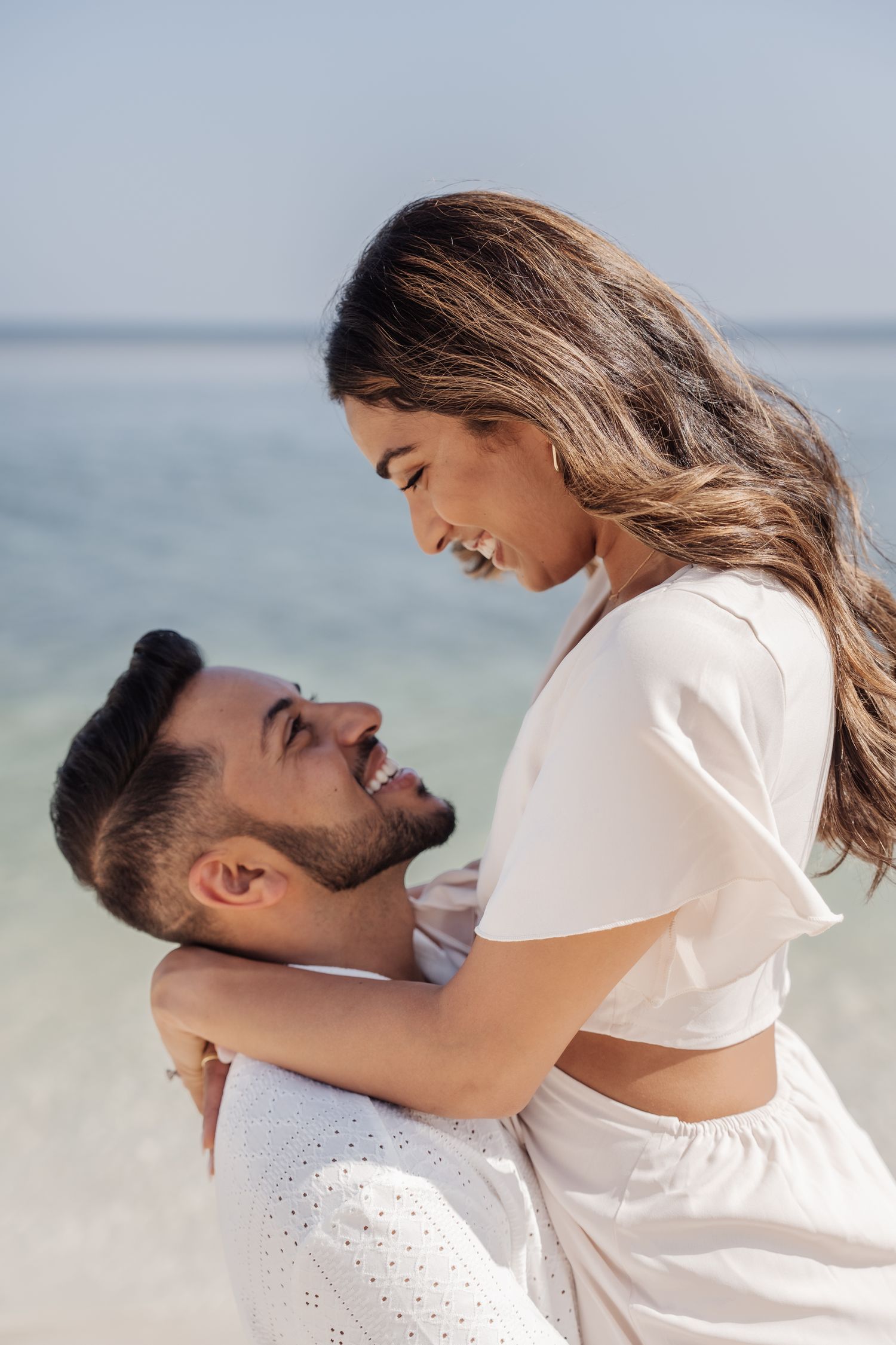 A loving couple shares an intimate moment on a sunny beach with the ocean as their backdrop.