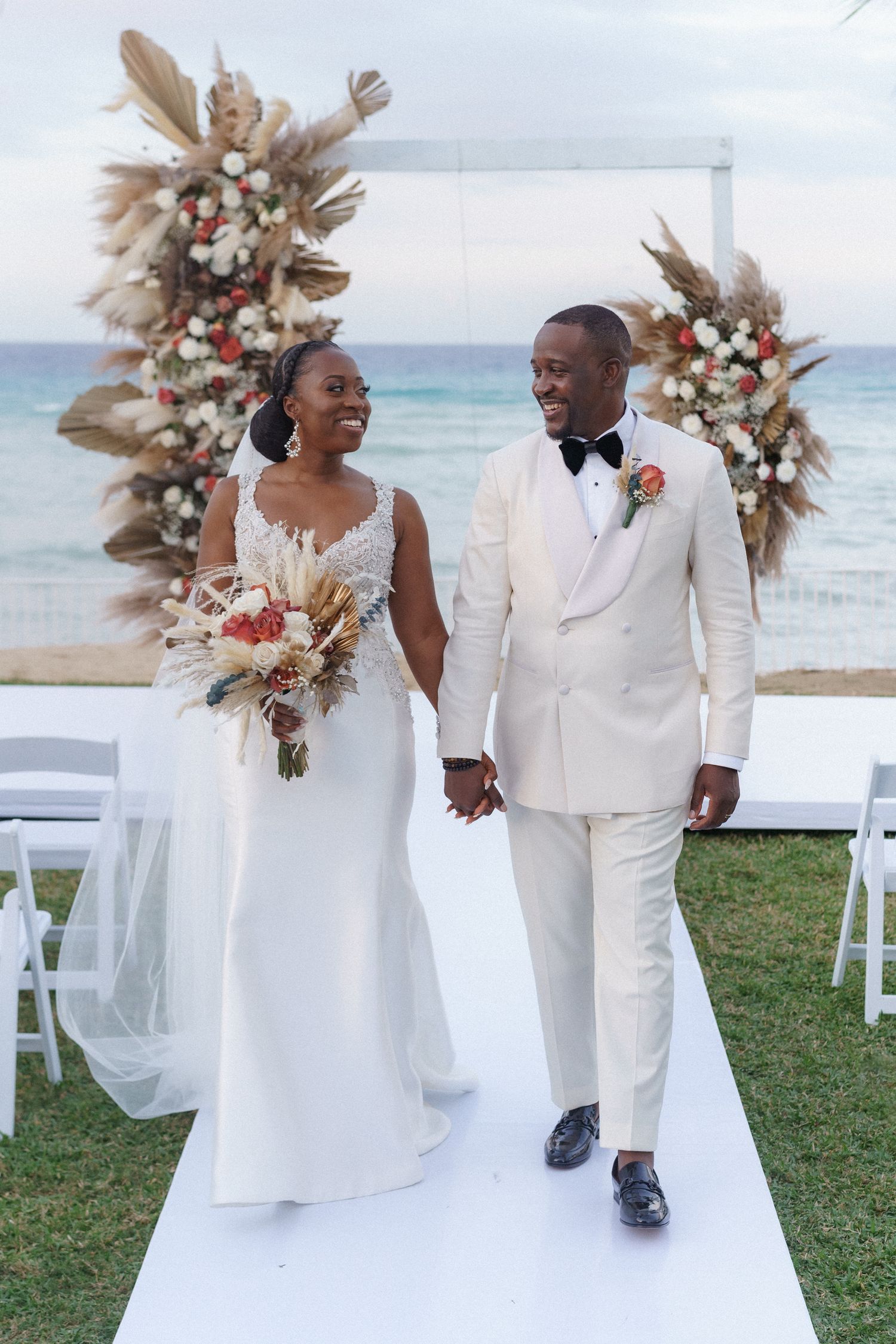 Beachside wedding ceremony with pampas grass floral arrangements and an ocean backdrop.