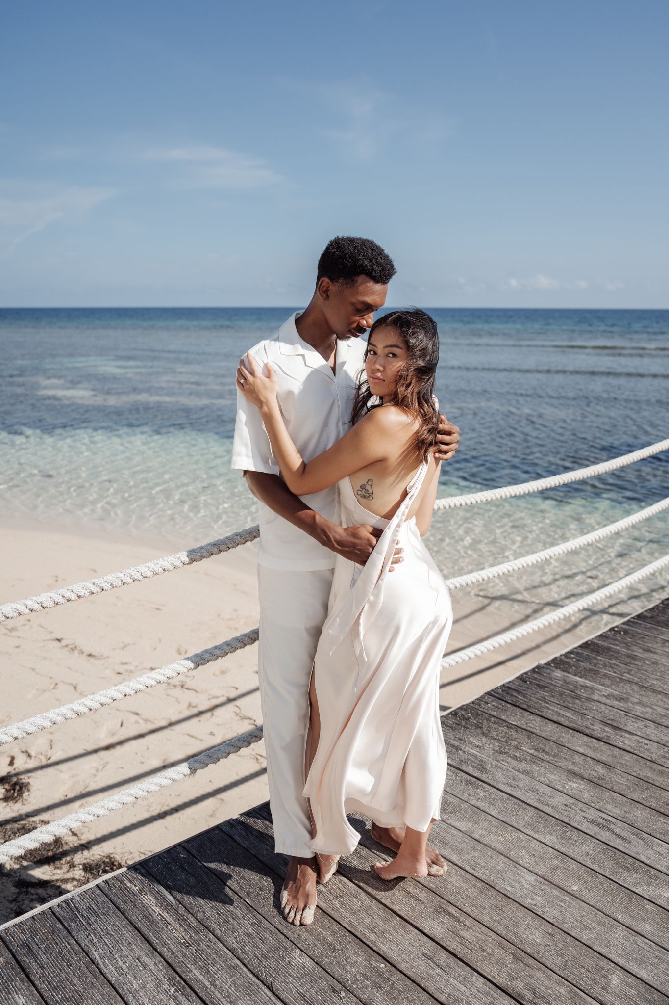 A couple shares an intimate moment on a wooden deck overlooking the ocean.