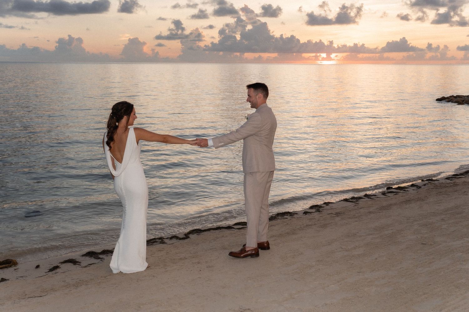 Couple holds hands on beach at sunset during destination wedding ceremony.