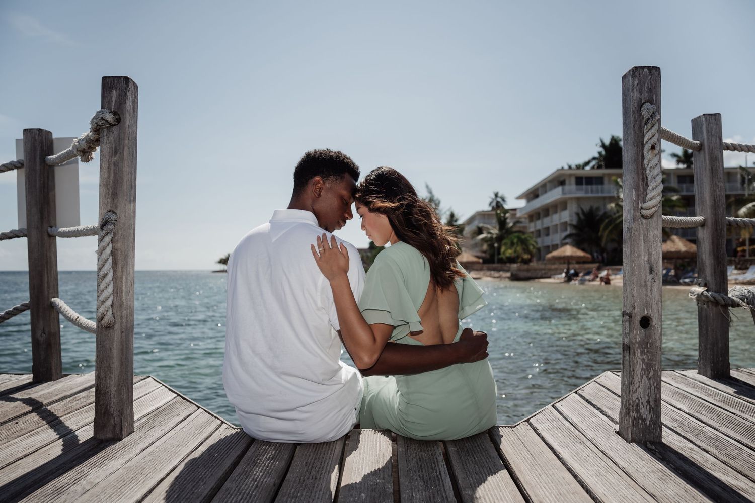 Intimate moment shared between couple sitting on wooden dock over turquoise waters.