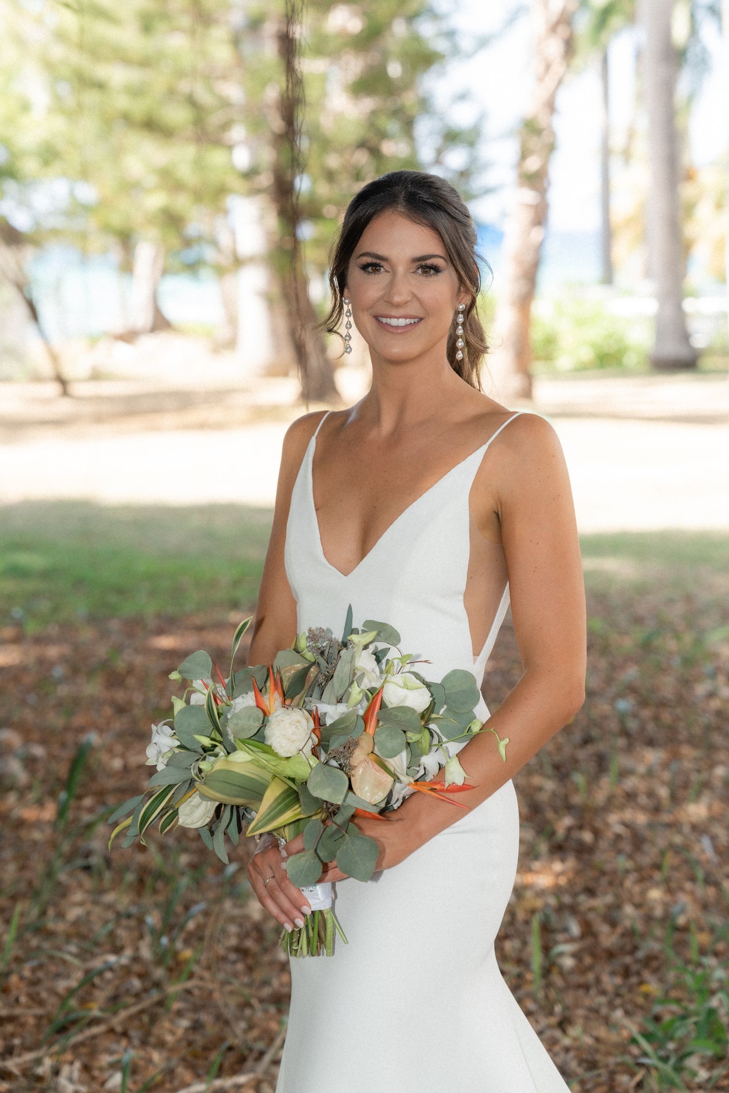Bride holding a eucalyptus and white flower bouquet poses in an elegant fitted wedding dress.