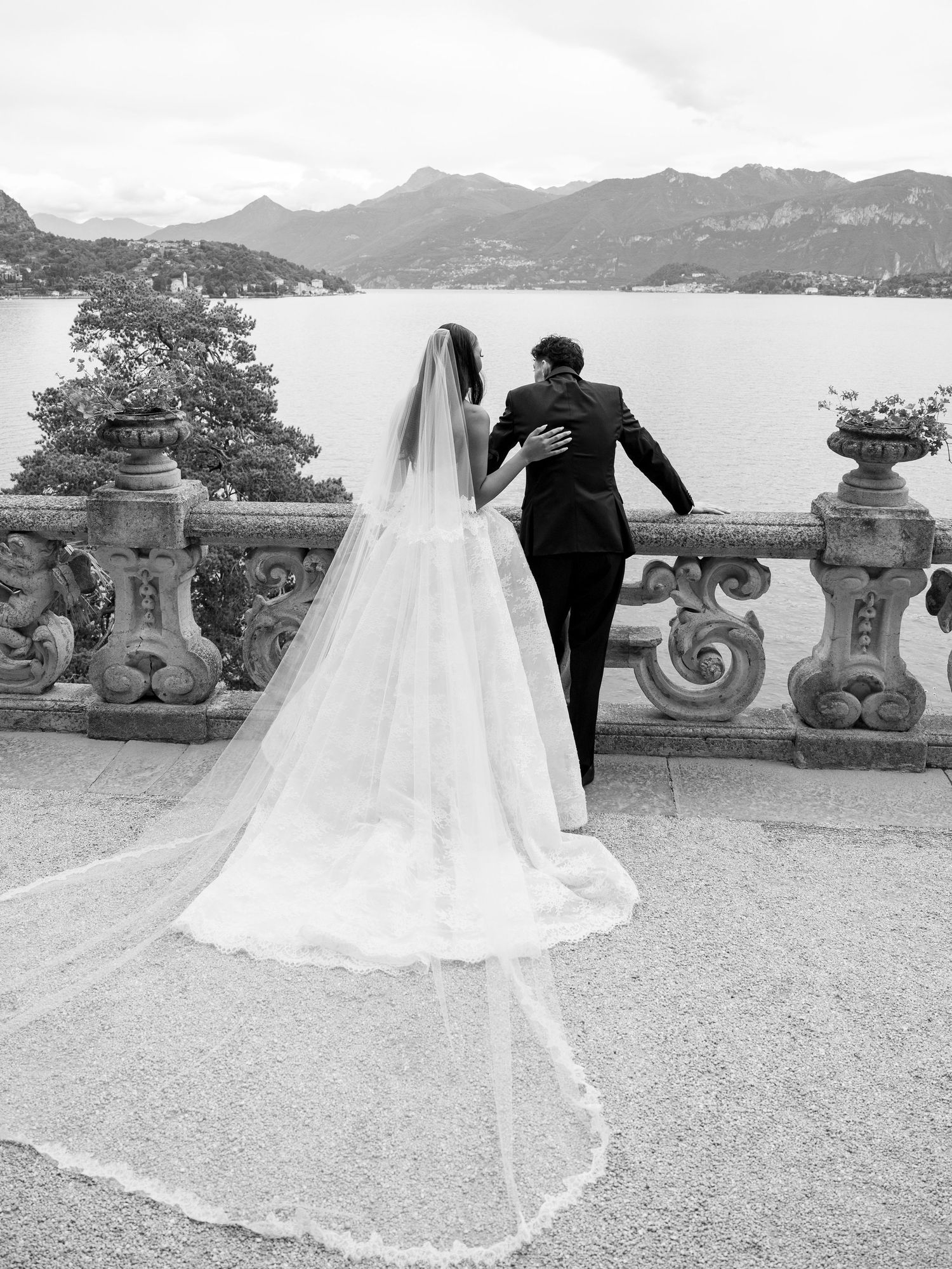 Elegant wedding couple poses against a scenic lake and mountain backdrop in black and white photography.