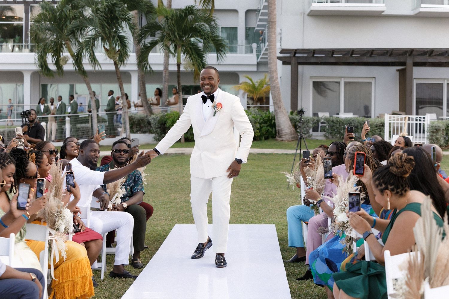 Wedding fashion show on an outdoor runway with palm trees and audience members watching in excitement.