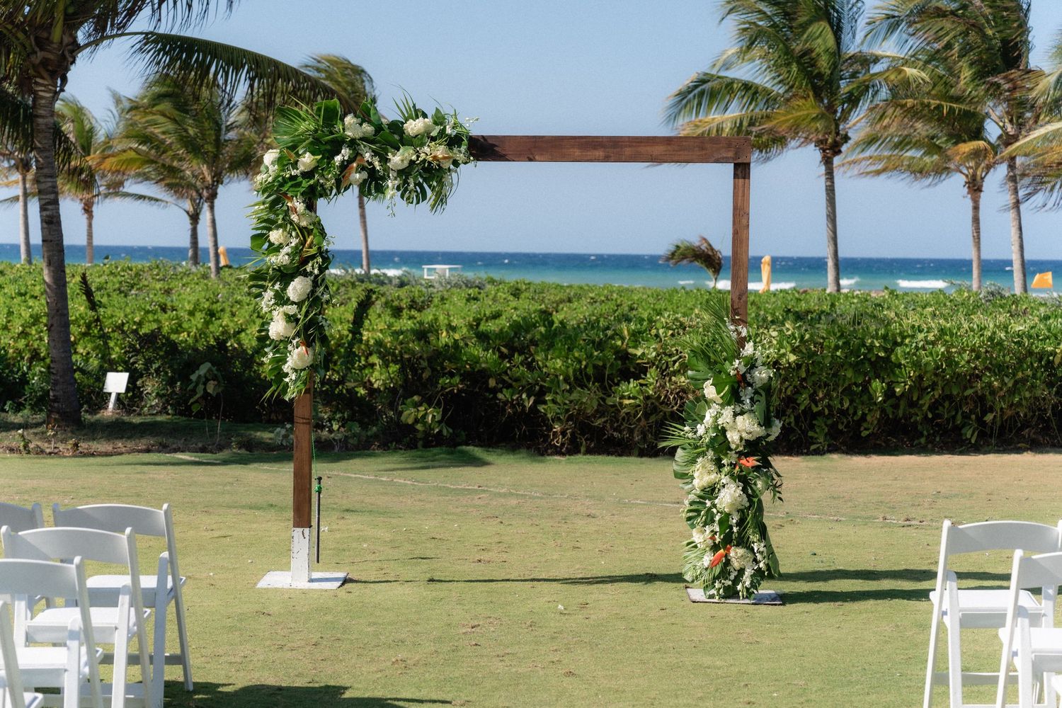 A beachfront wedding arch decorated with white flowers and greenery overlooking the ocean.