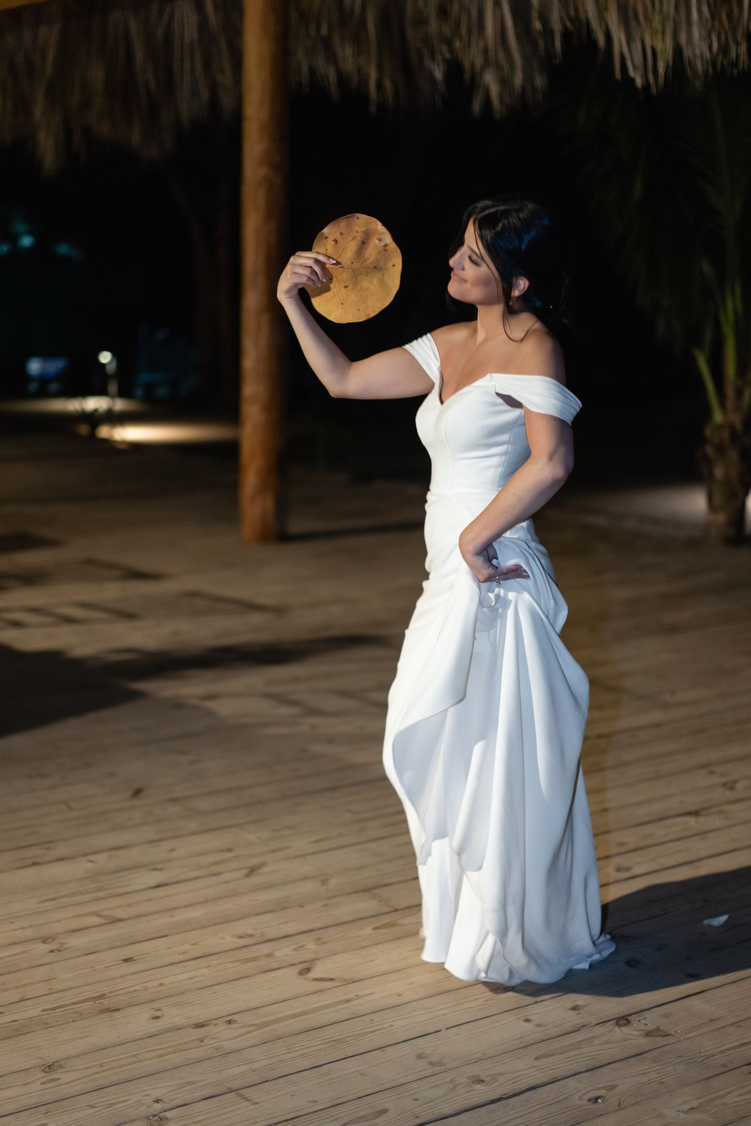 Dancing scene on wooden deck under thatched roof pavilion at night.
