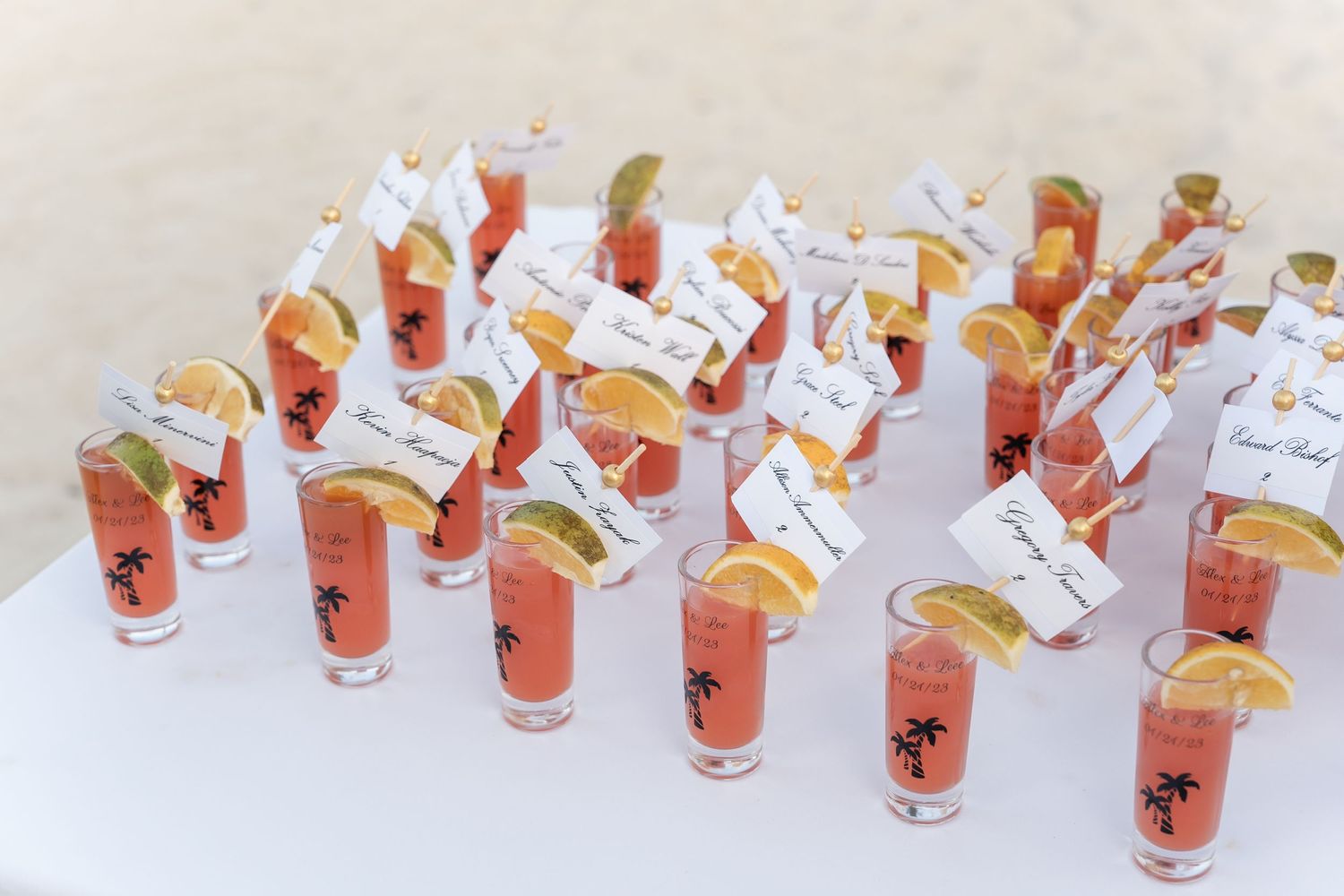 Pink signature cocktails in small glasses arranged with name tags as wedding favors.