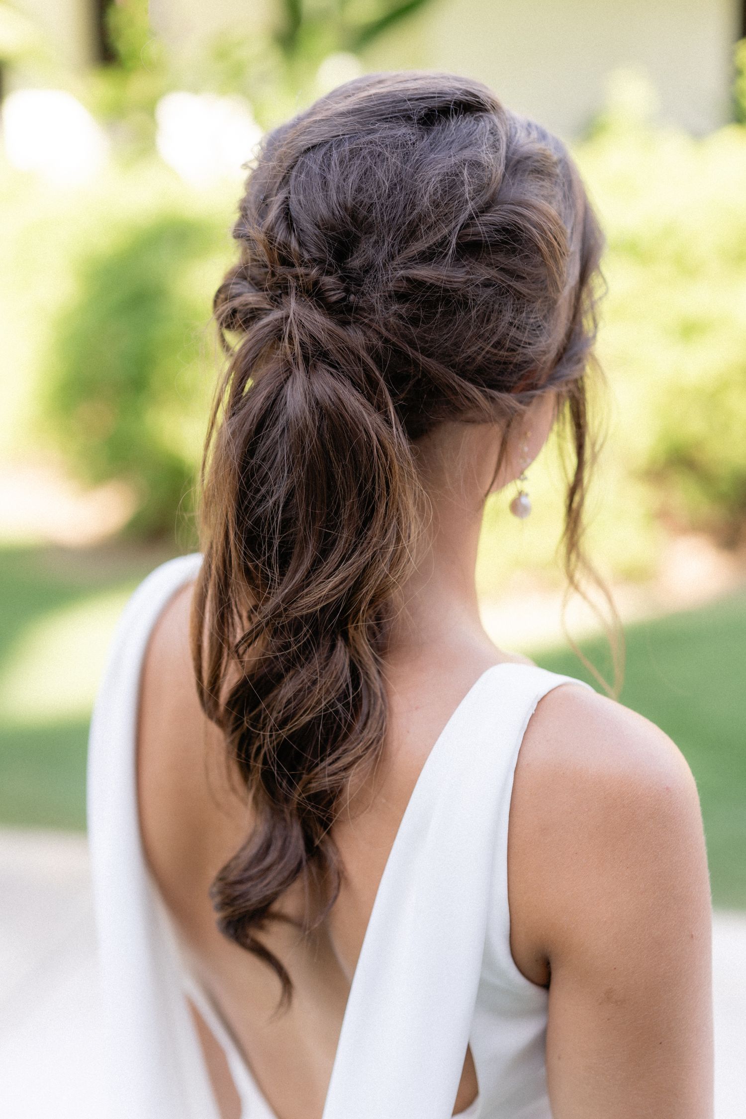 Romantic bridal hairstyle featuring loose waves pulled into elegant low ponytail with soft tendrils.