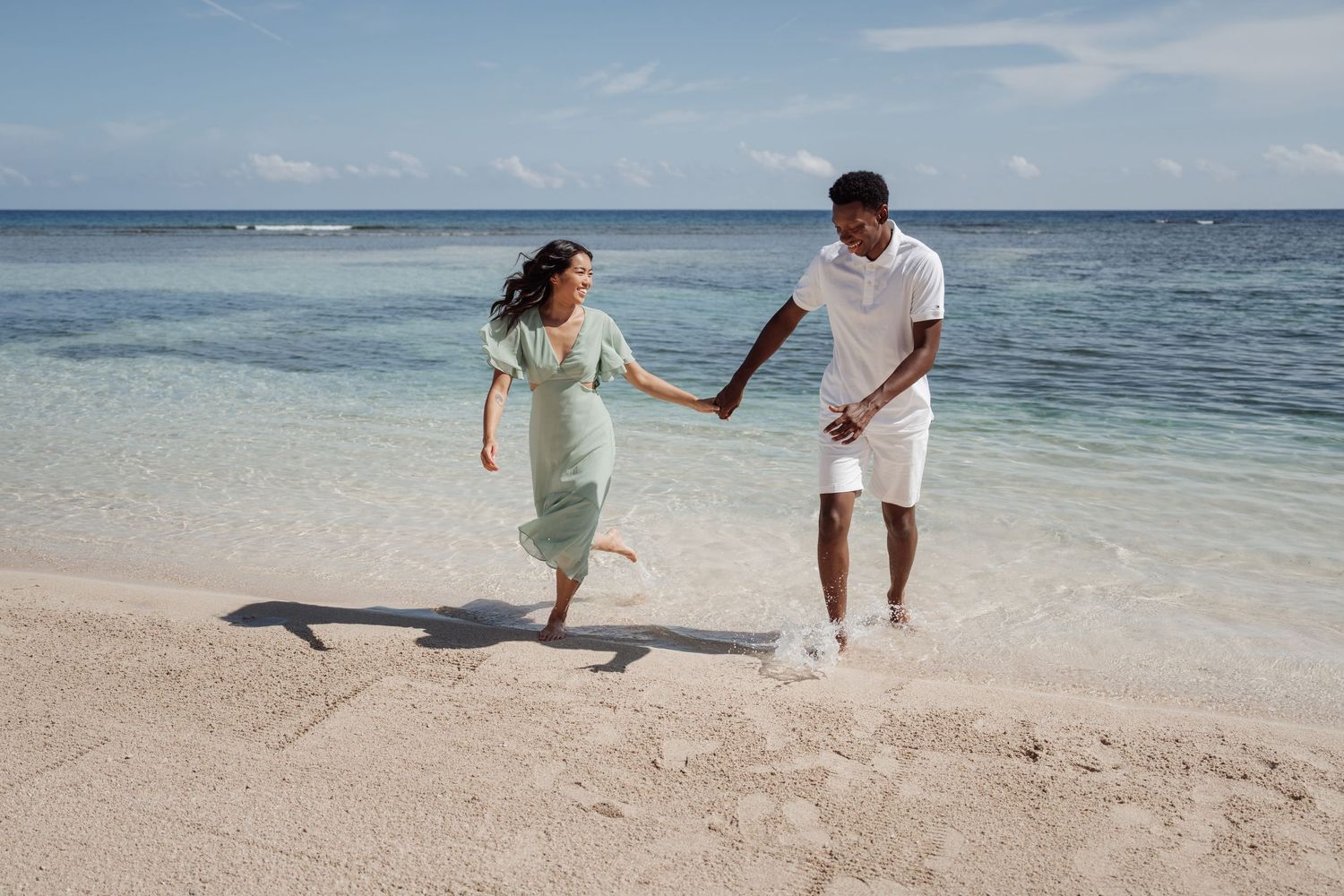 A couple runs playfully together on a pristine beach with turquoise ocean waters in the background.