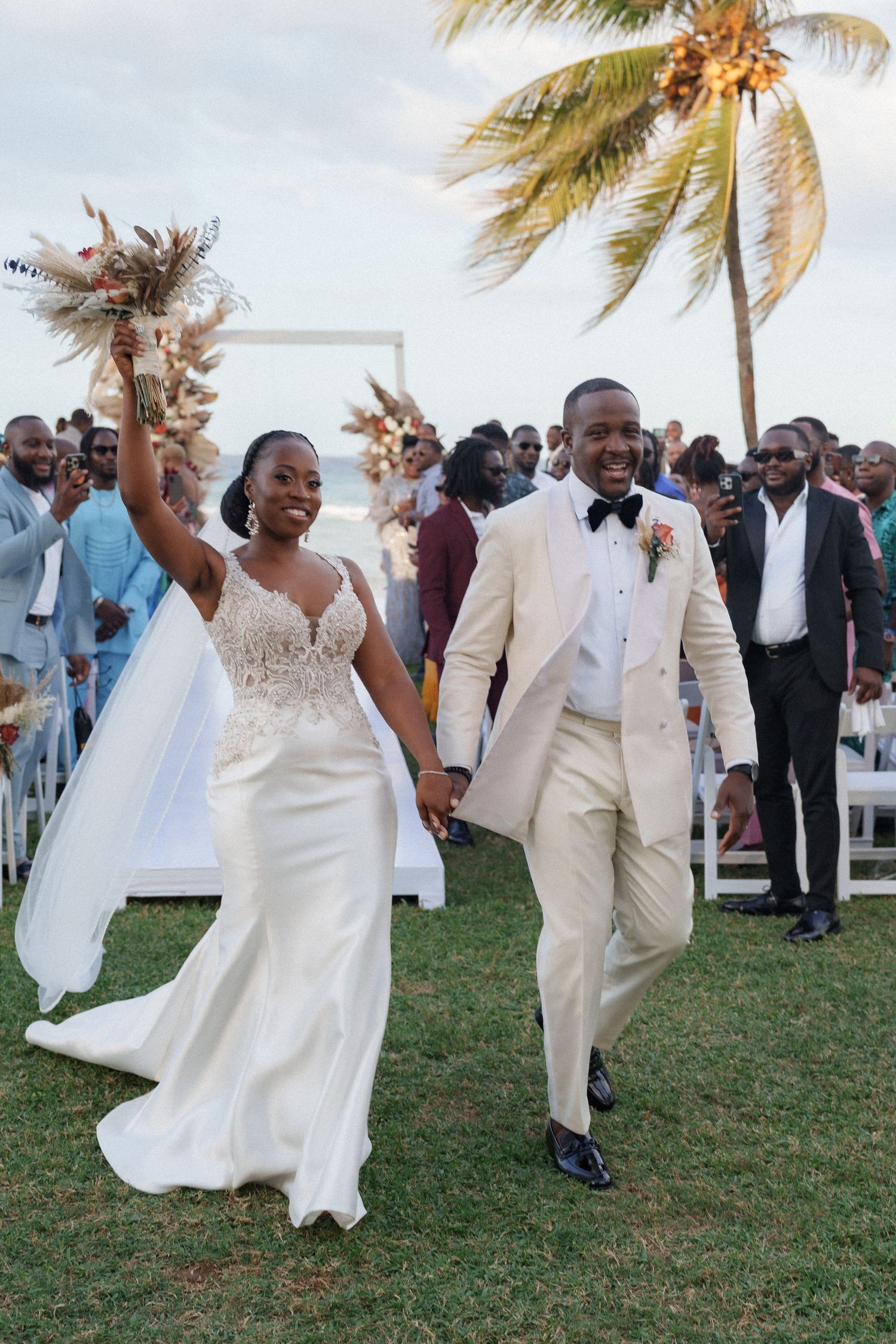 Celebratory wedding exit on a grassy lawn with palm trees and ocean backdrop.