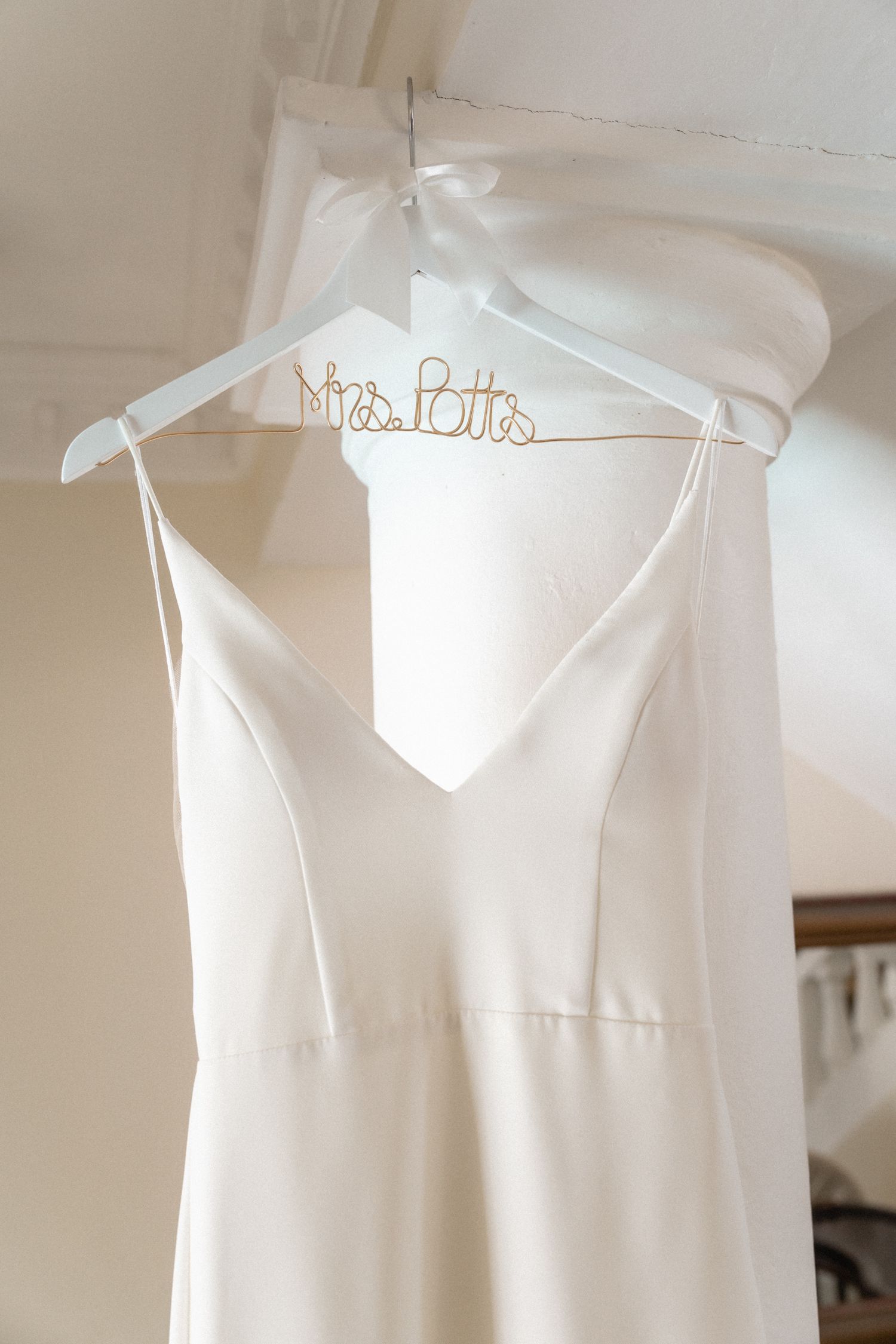White wedding dress on personalized bridal hanger displayed against light wall.