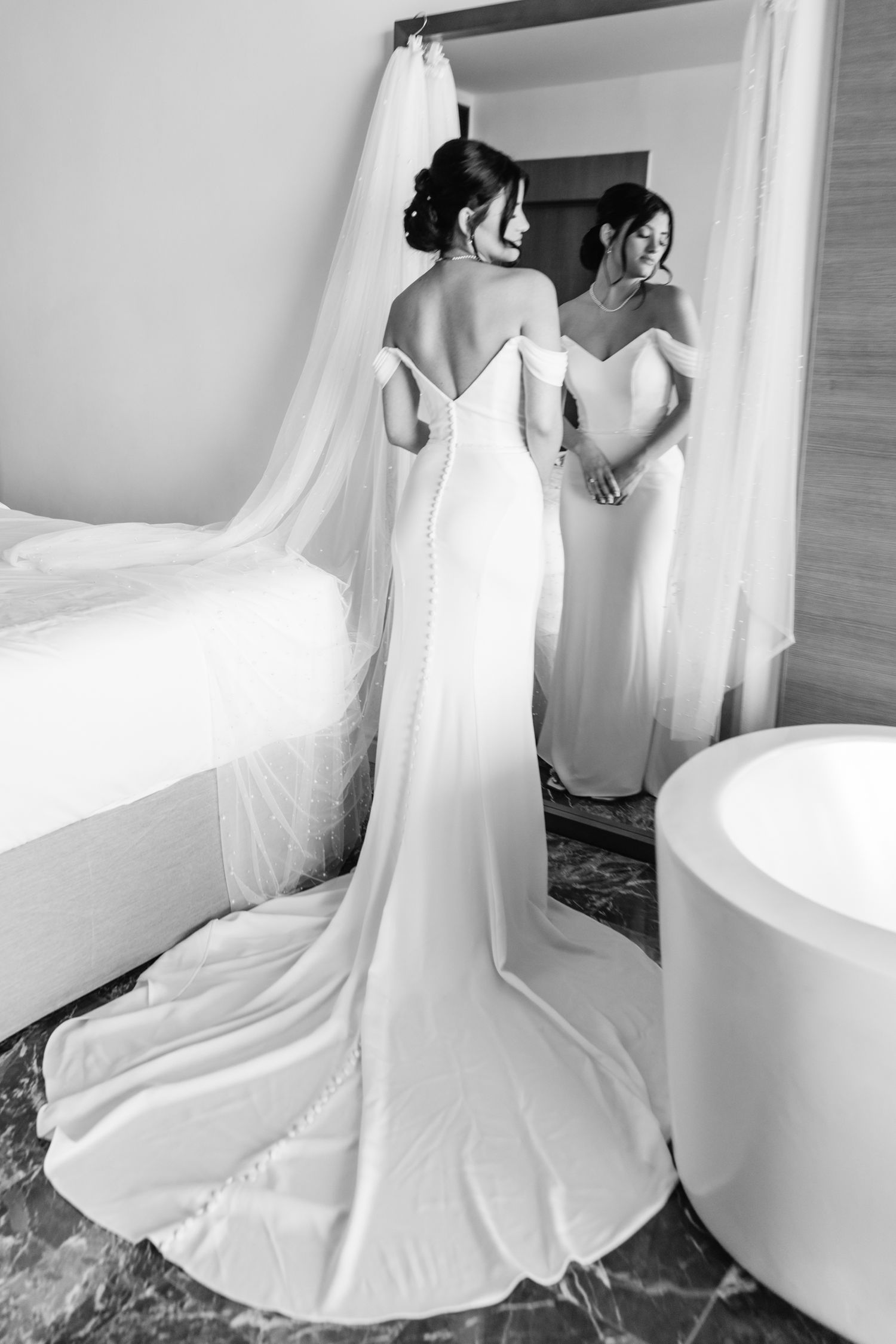 Elegant bridal gown with dramatic train captured in black and white mirror reflection.