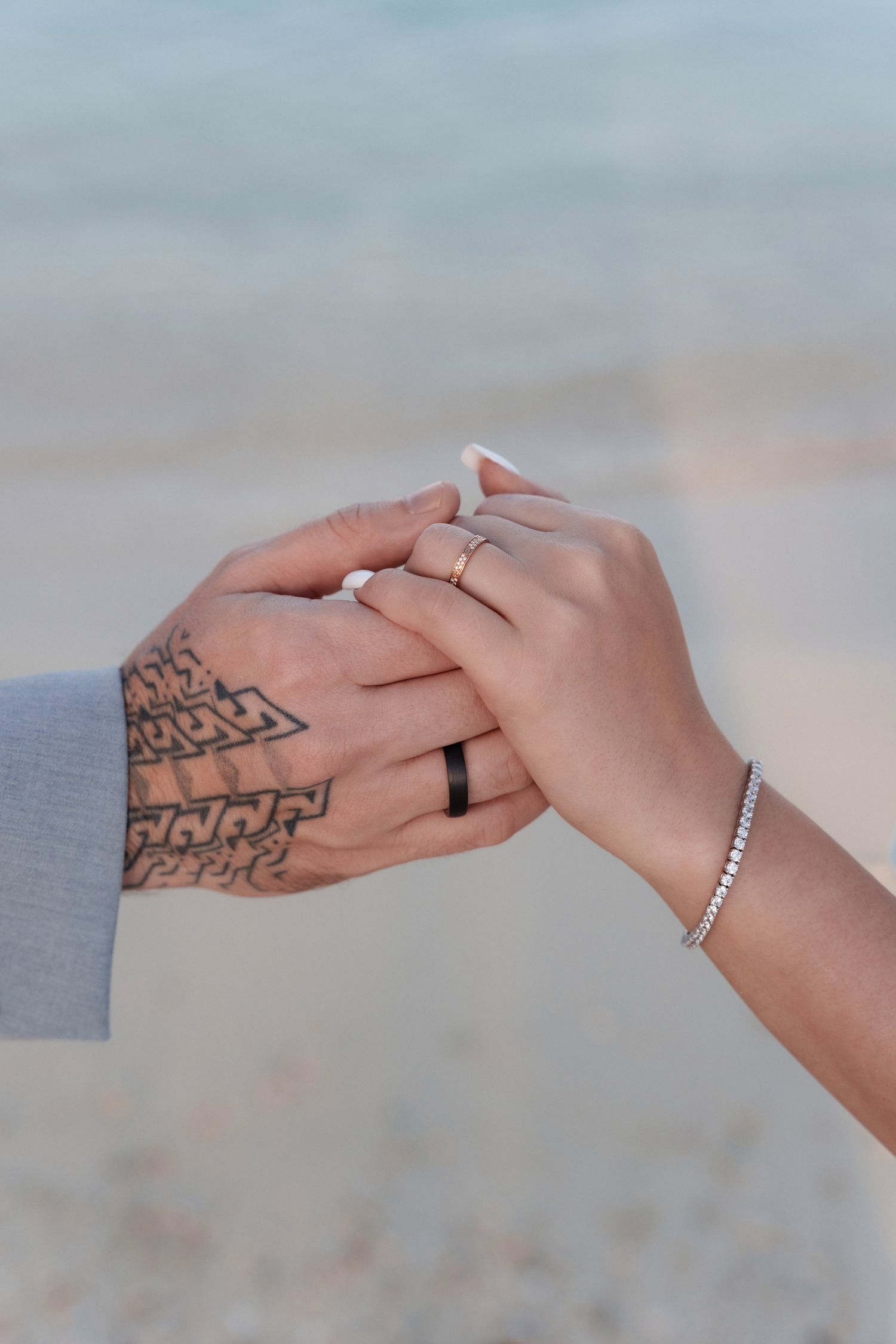 Close-up of two hands with wedding rings and a tattoo intertwined on beach setting.