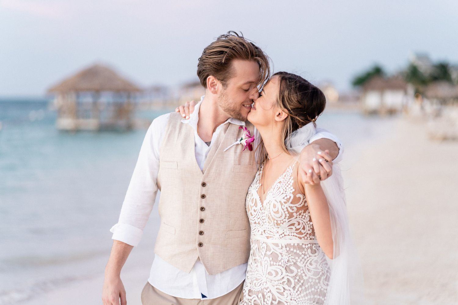 A tender moment captured on a tropical beach with beige vest and lace dress details.