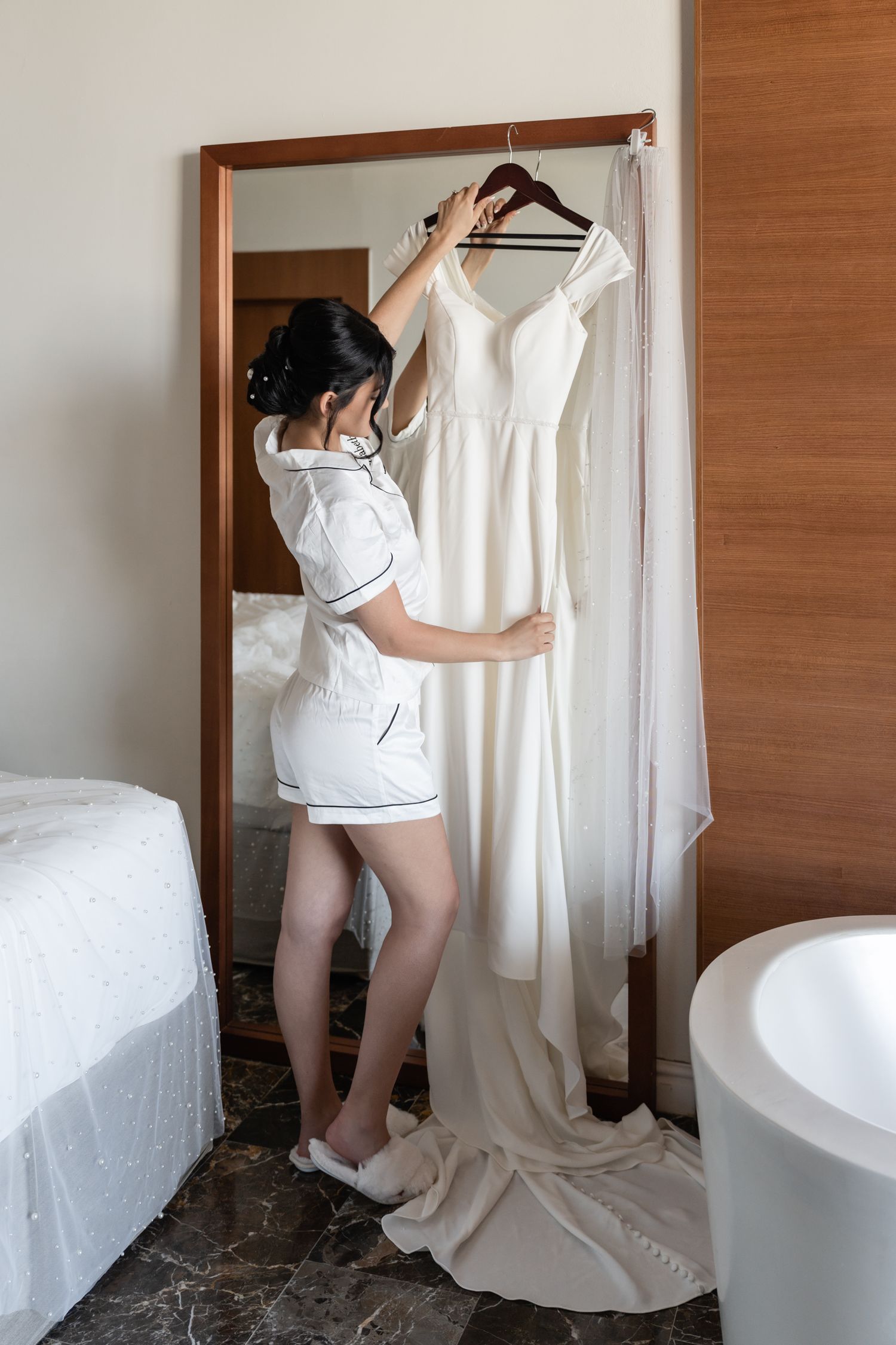 Wedding dress preparation scene with white gown hanging in hotel room mirror.
