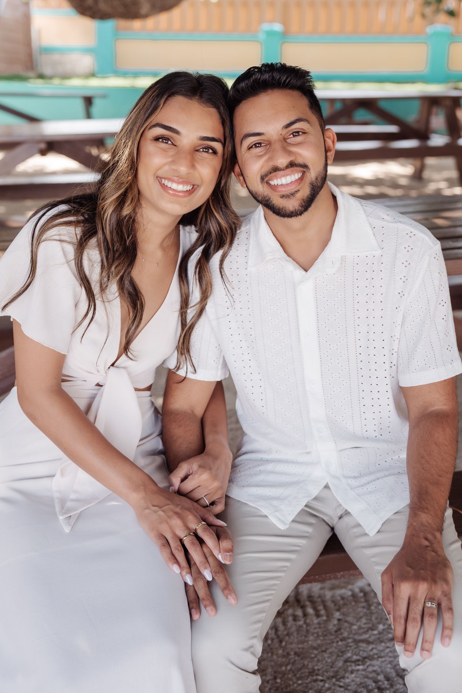 Couple in matching white outfits sitting together on a turquoise bench.