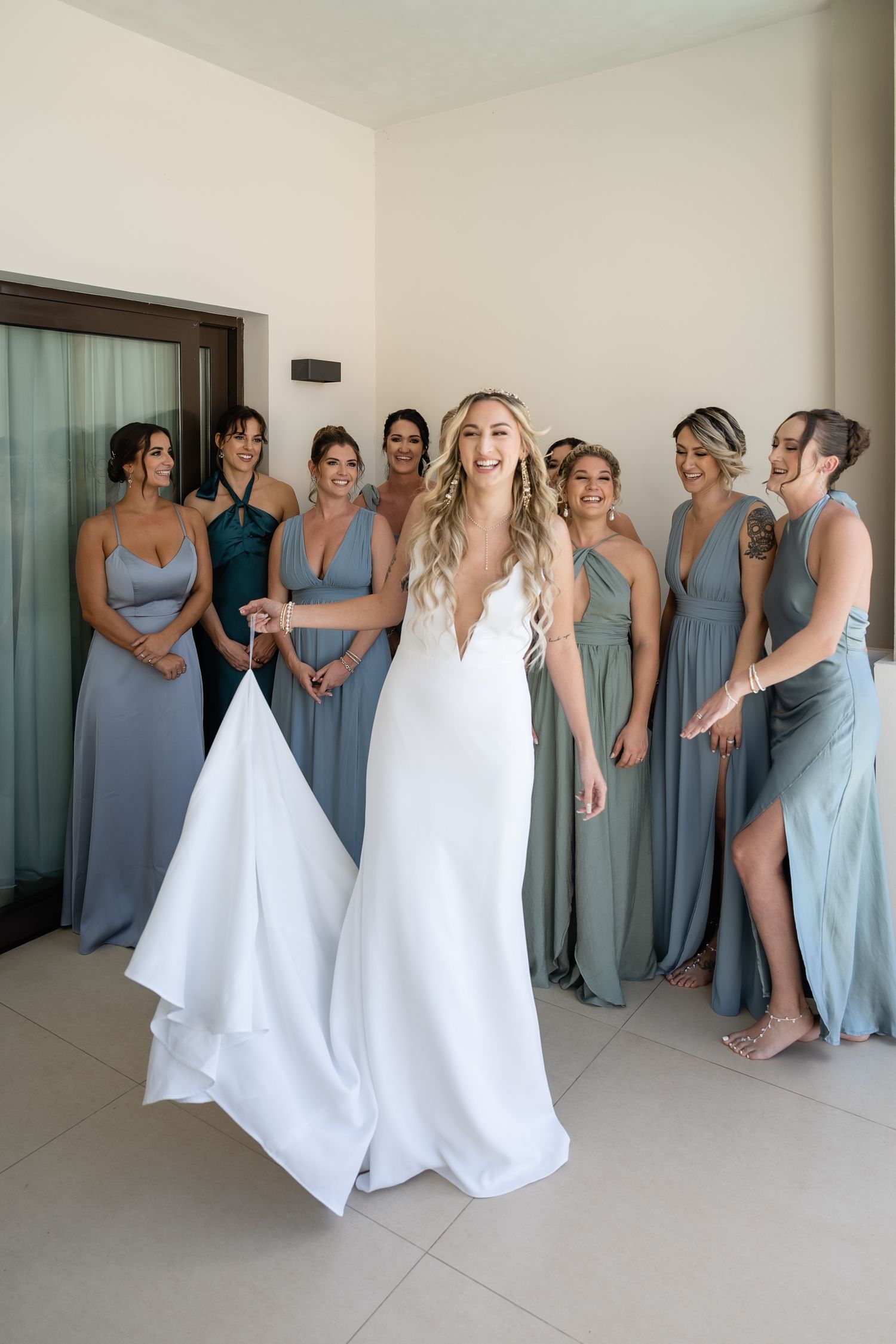 A wedding party poses together with bridesmaids in blue dresses surrounding someone in a white gown.