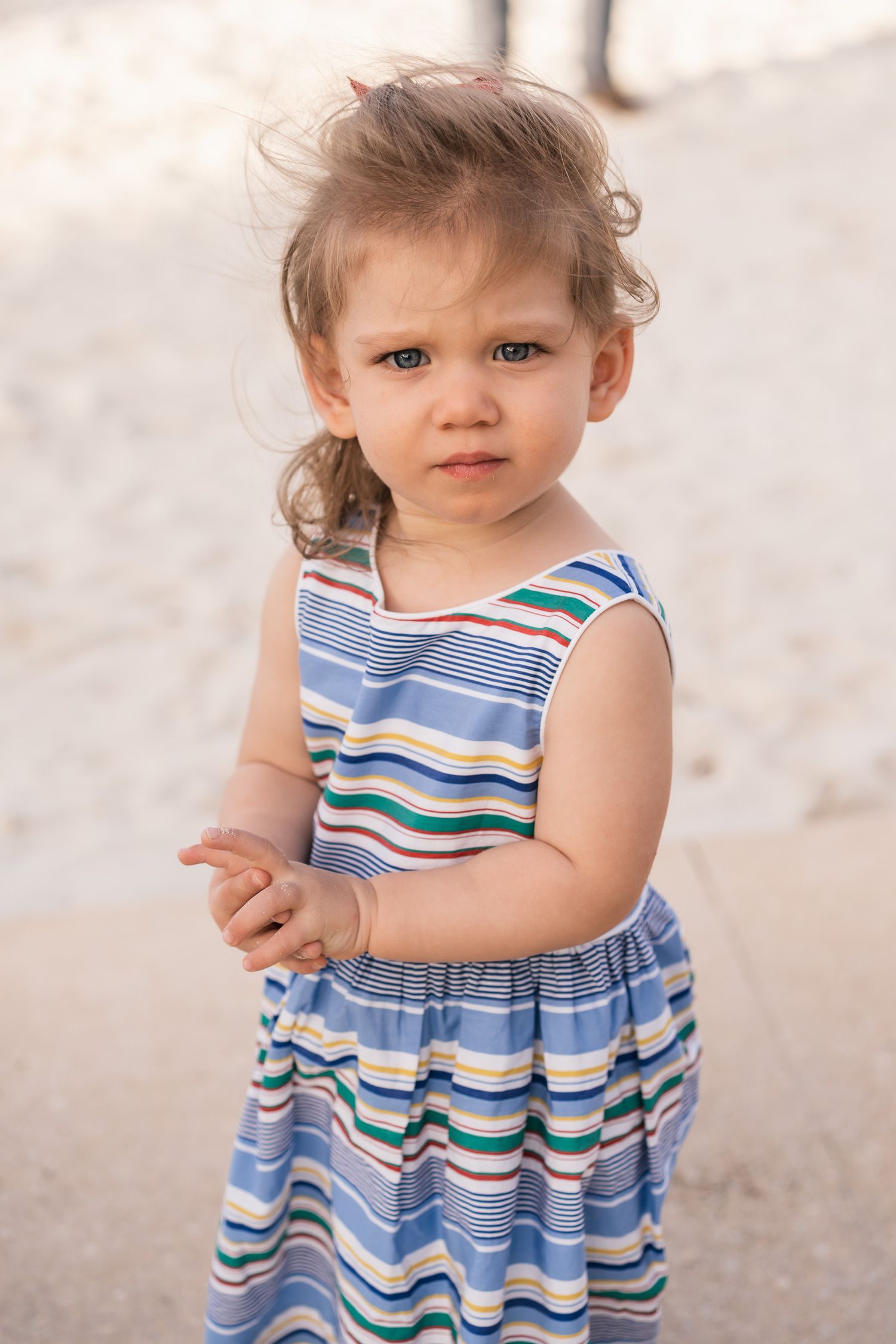 Toddler in blue striped summer dress looking at camera with curious expression.