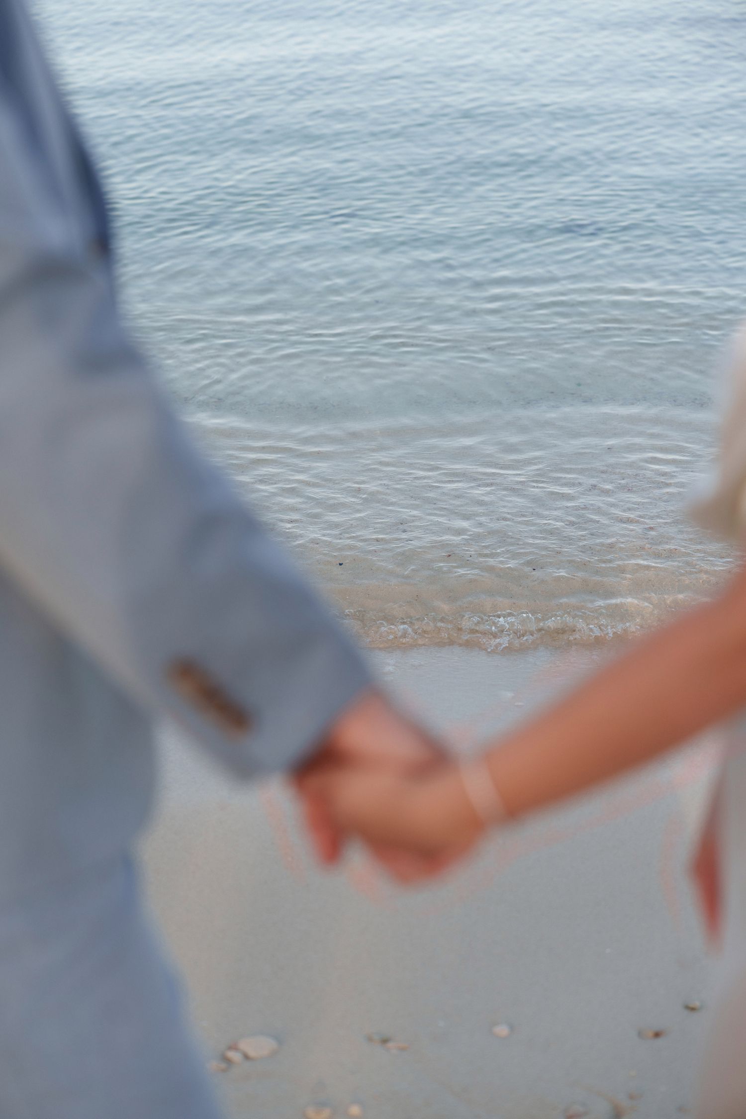Close-up of clasped hands against ocean waves and sandy beach background.