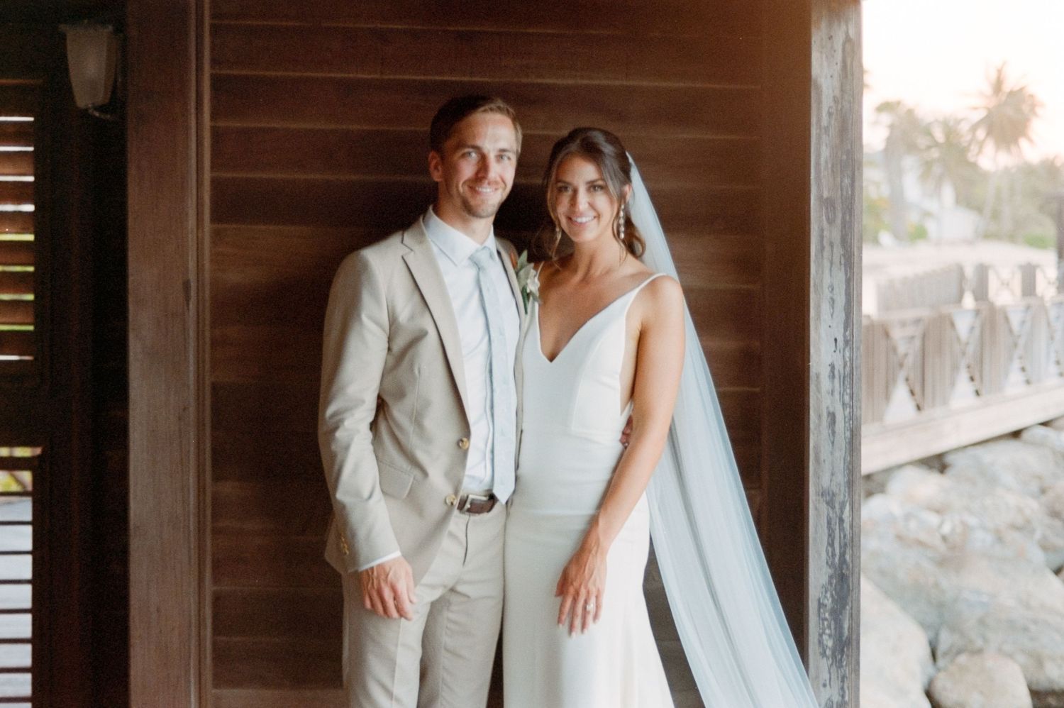 A couple in light-colored wedding attire poses in a rustic wooden doorway.