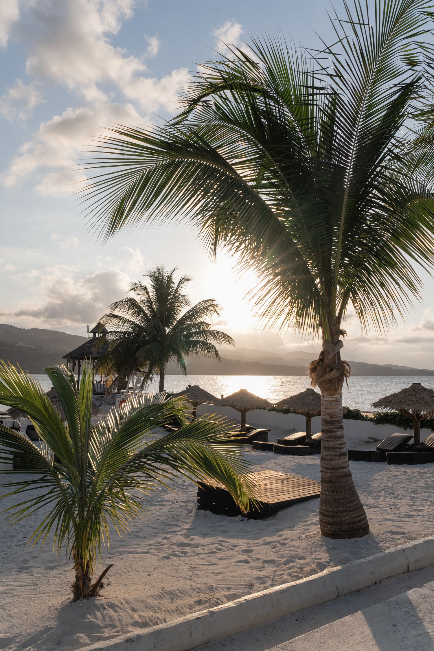 Palm trees frame a sunset view over a tropical beach with lounge chairs.