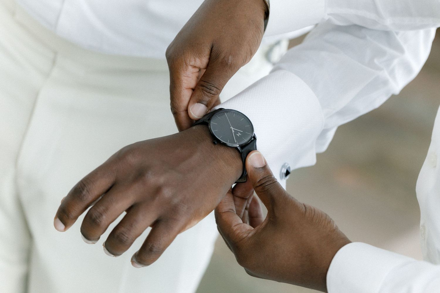 Close-up of hands fastening luxury watch with white formal attire.