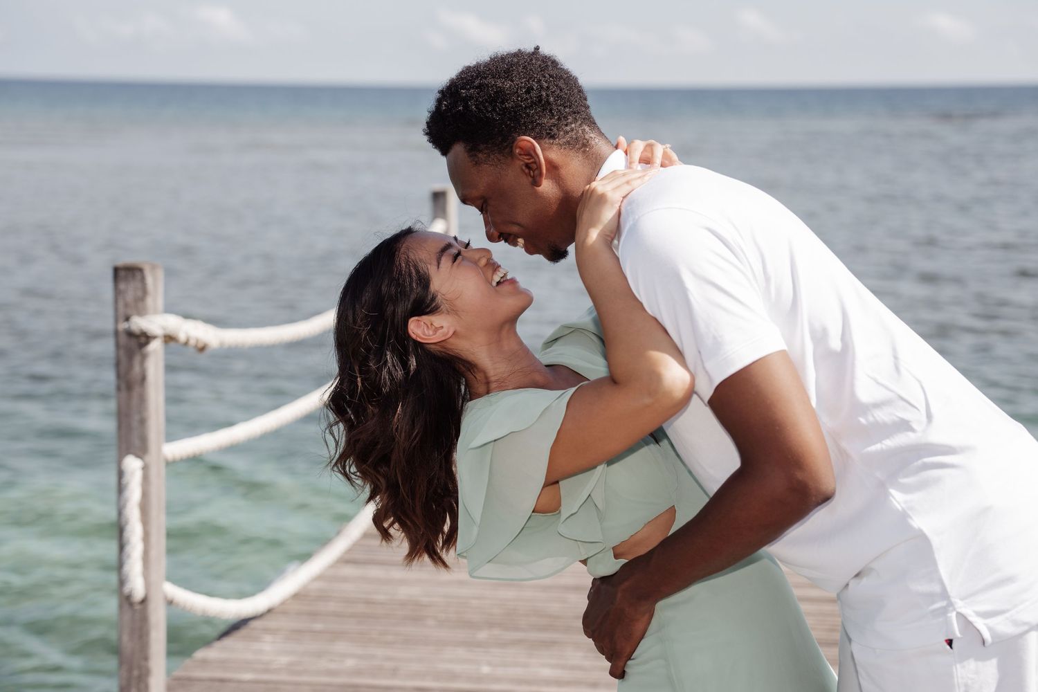 A romantic dip pose on a wooden pier with ocean views.