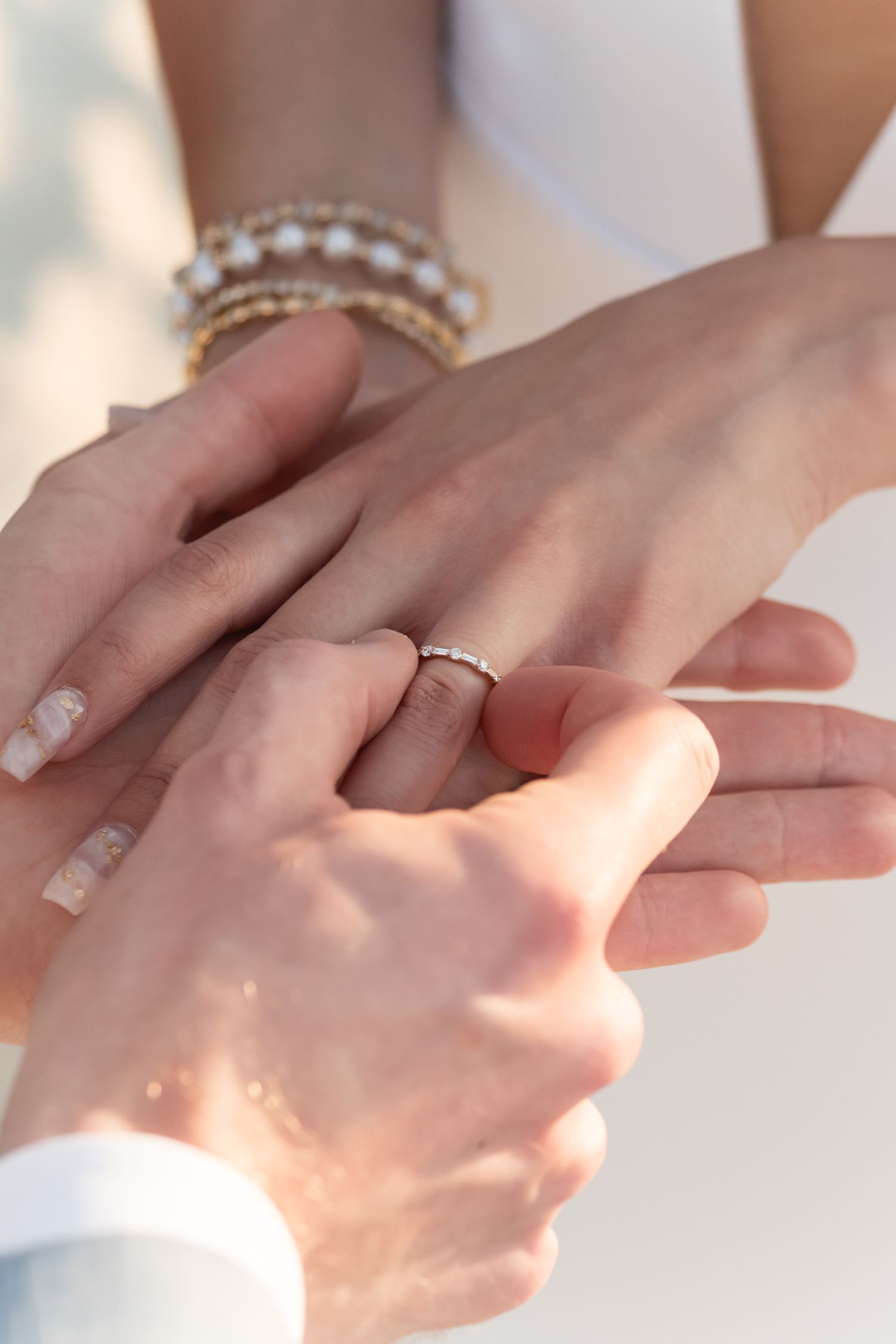 Close-up of hands exchanging wedding rings with sparkly bracelets.