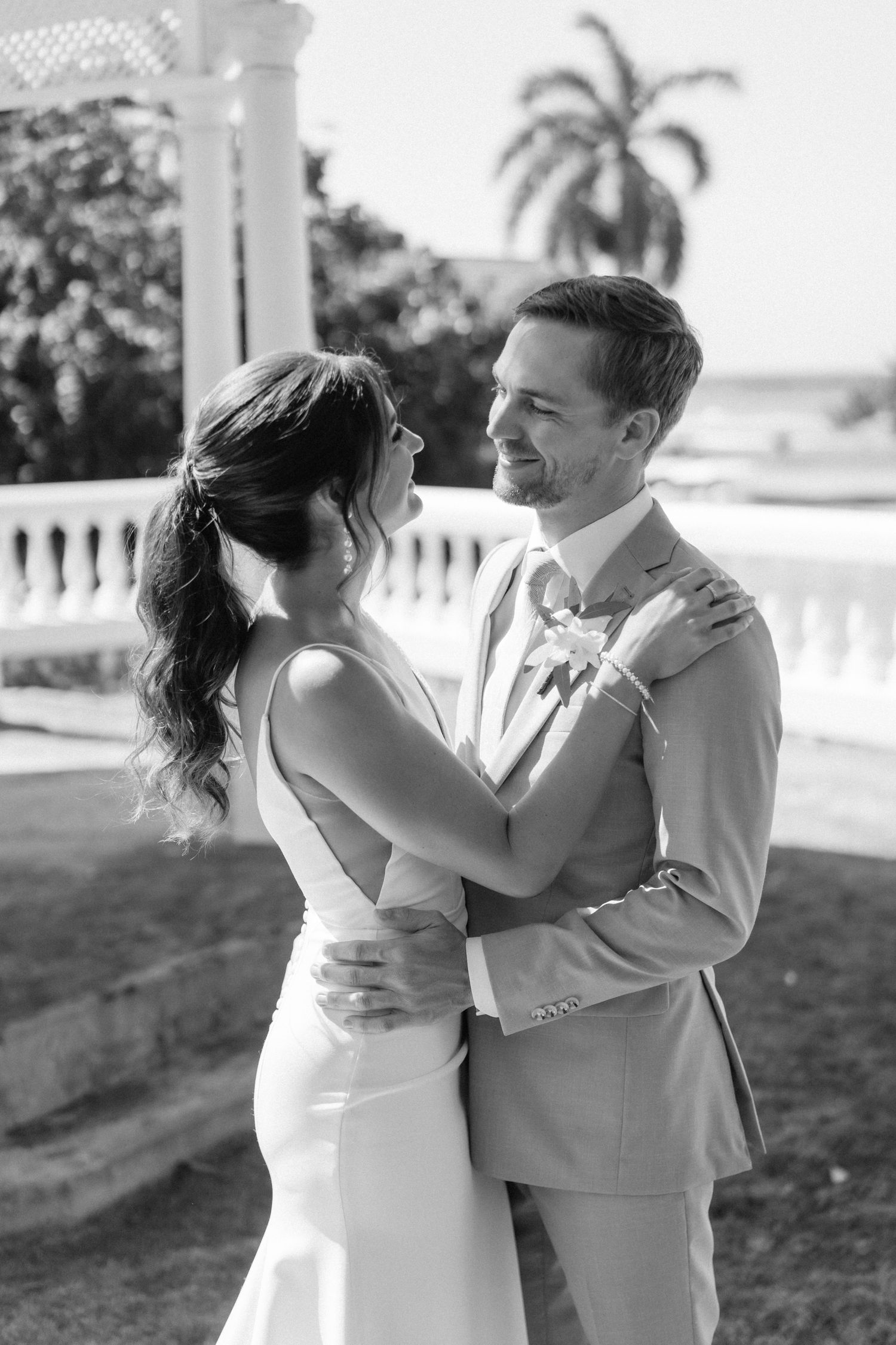 A black and white romantic portrait of a couple in wedding attire under a gazebo.