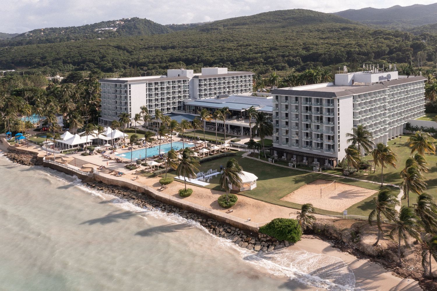 Beachfront resort hotel with multiple swimming pools and palm trees along the coastline.