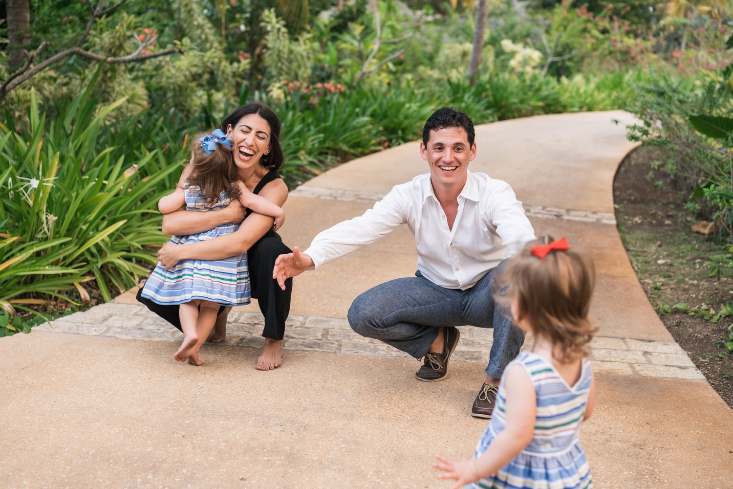 Family playing and laughing together on a winding garden path surrounded by tropical plants.