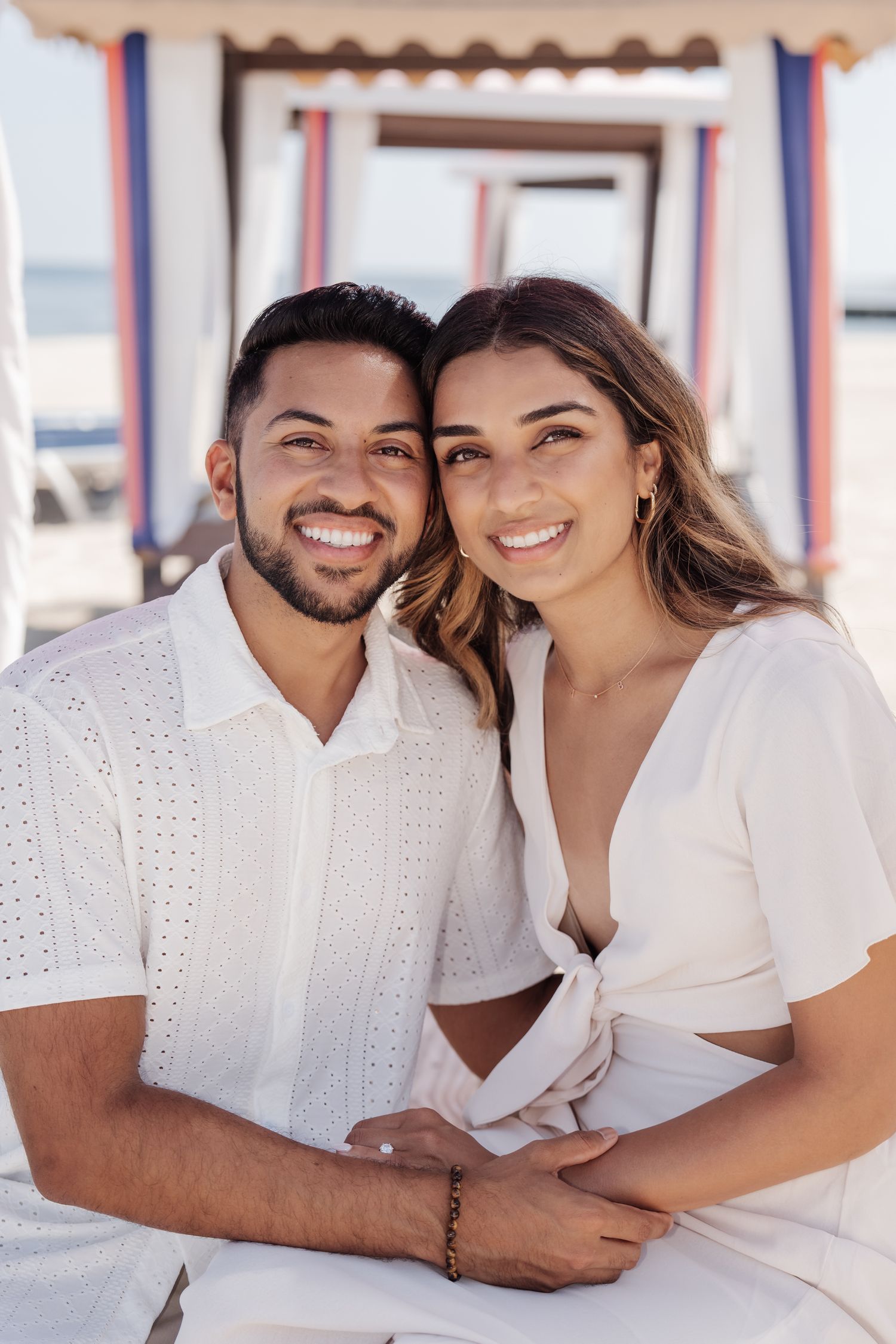 A happy couple embraces under a decorative beach cabana with striped awning.