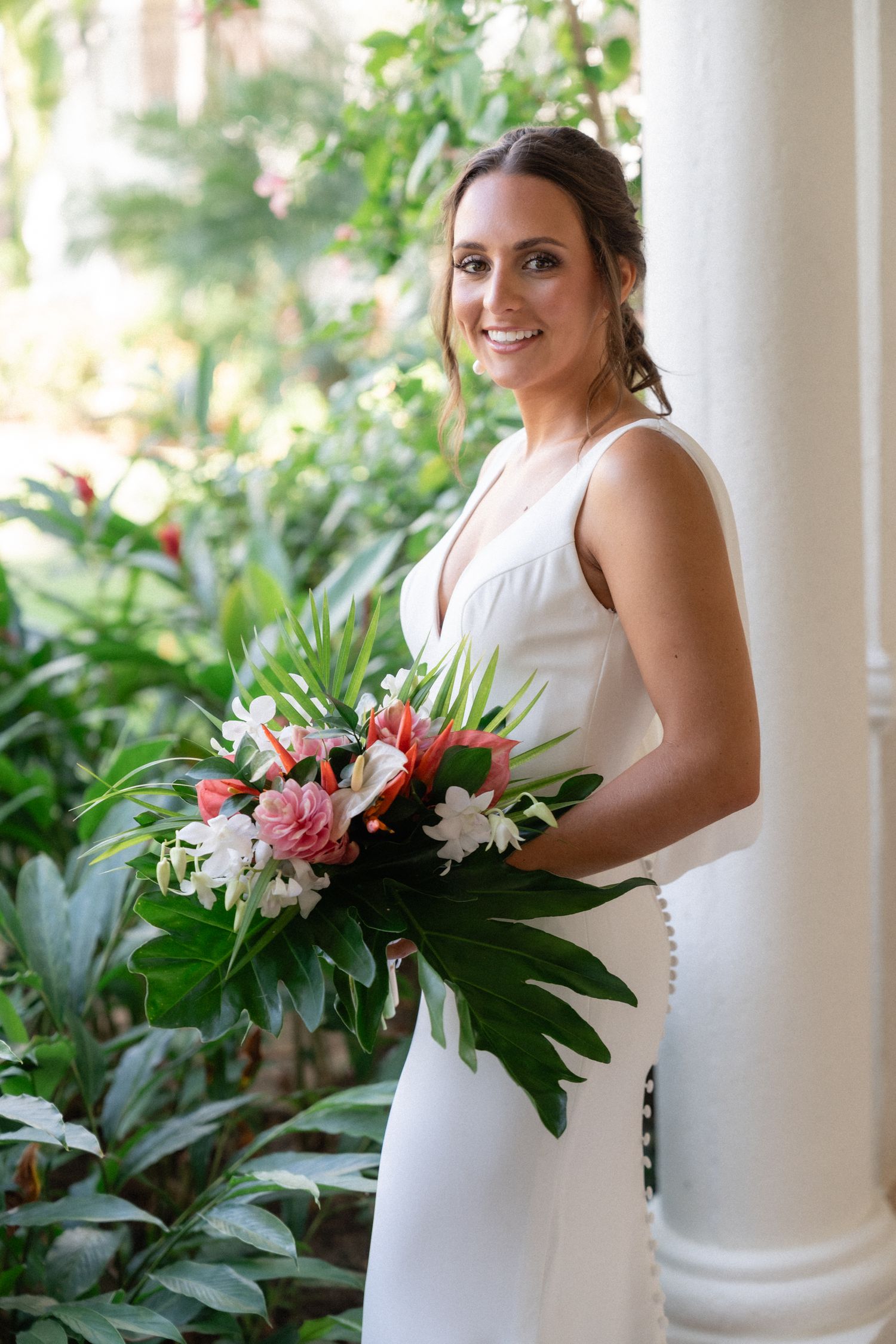 Elegant tropical wedding bouquet with white and pink flowers against lush garden backdrop.