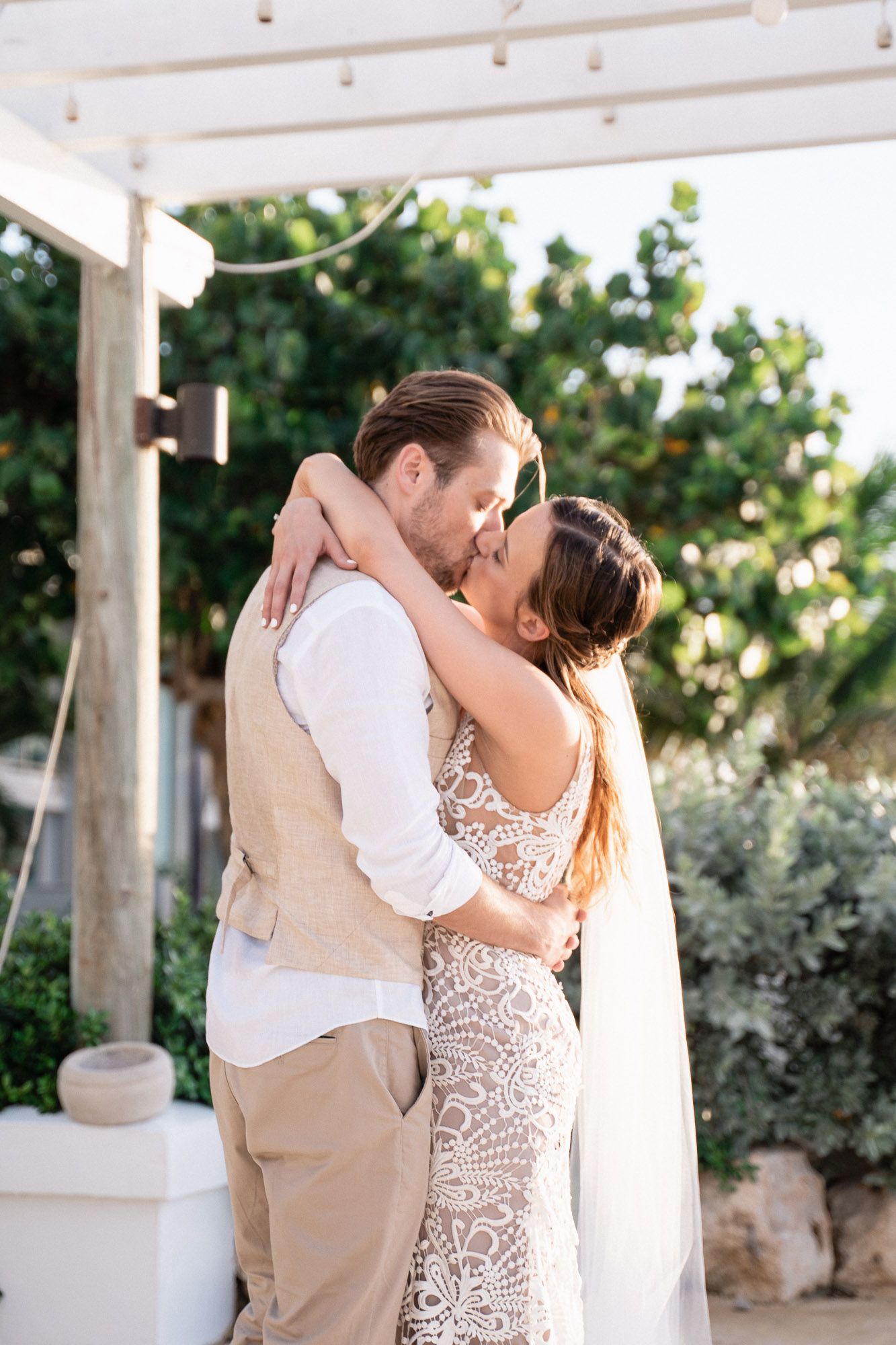 A romantic moment captured under a white pergola with lace dress details and casual beige attire.