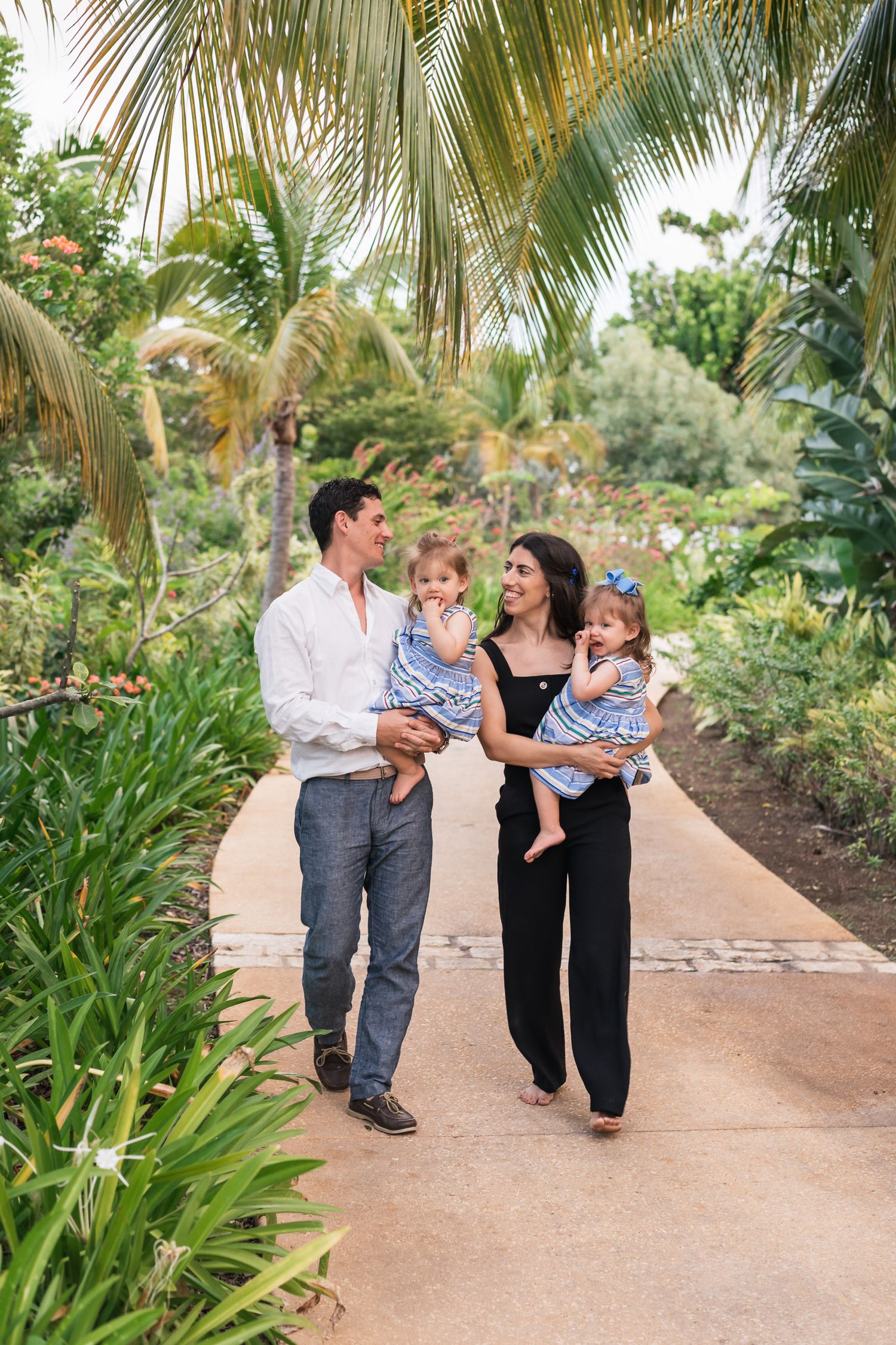 Family walking together on a palm-lined pathway in tropical garden setting.